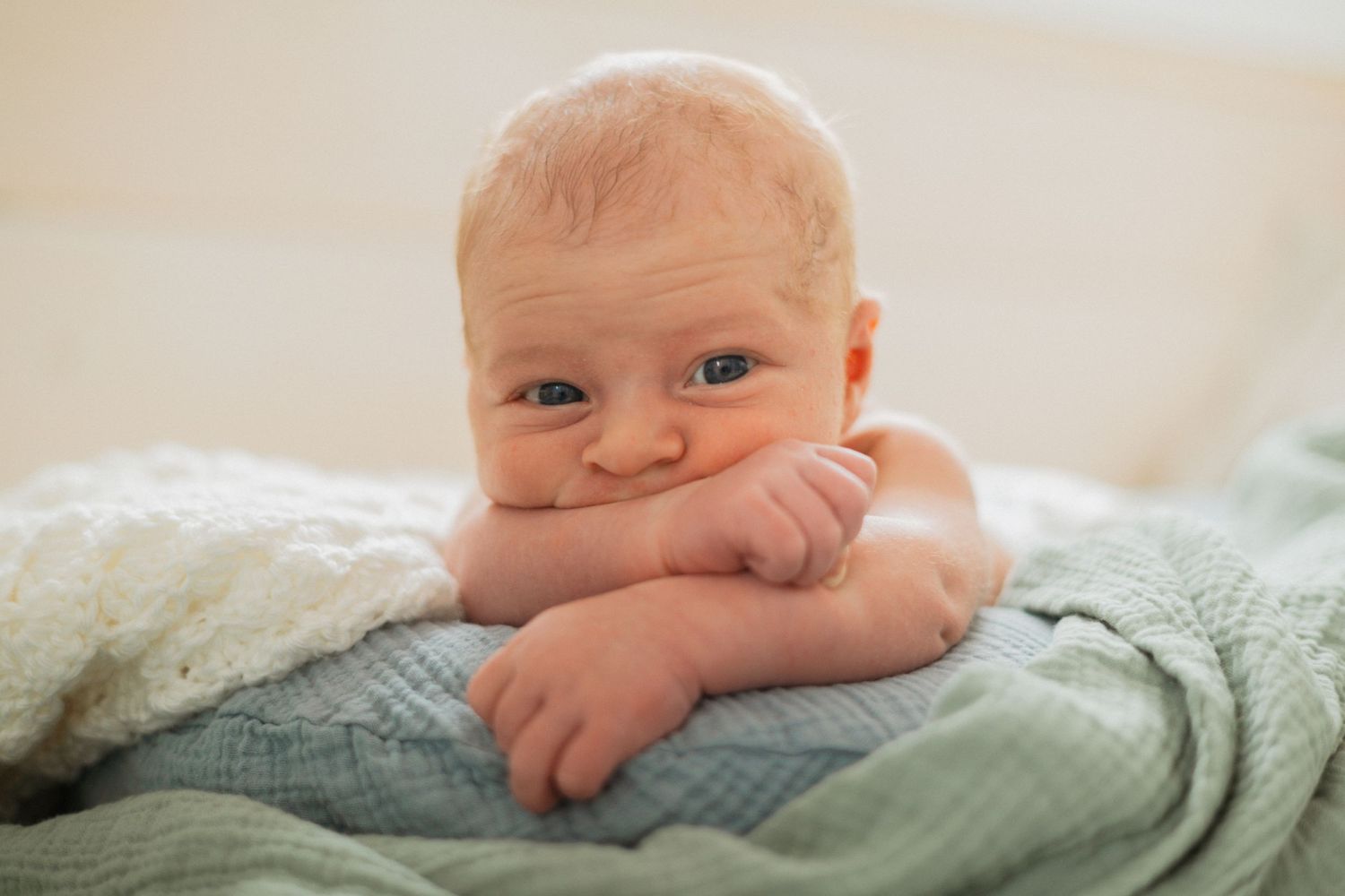 Bright and cozy portrait of a newborn baby resting on a soft, layered blanket, gazing curiously with wide eyes and a sweet expression.