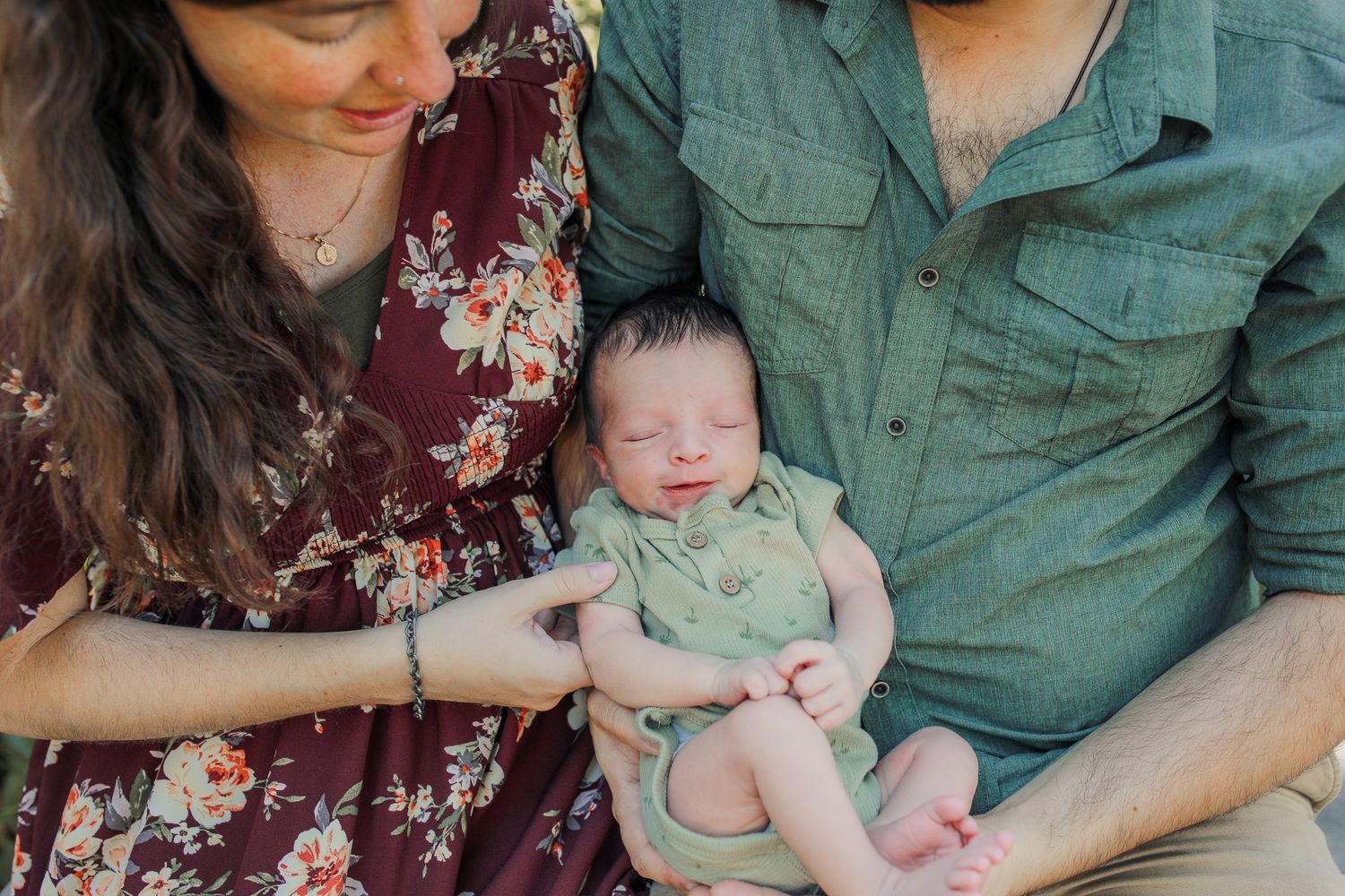 Newborn baby cradled by loving parents, dressed in soft greens, evoking warmth, tenderness, and beauty of family moments captured naturally.