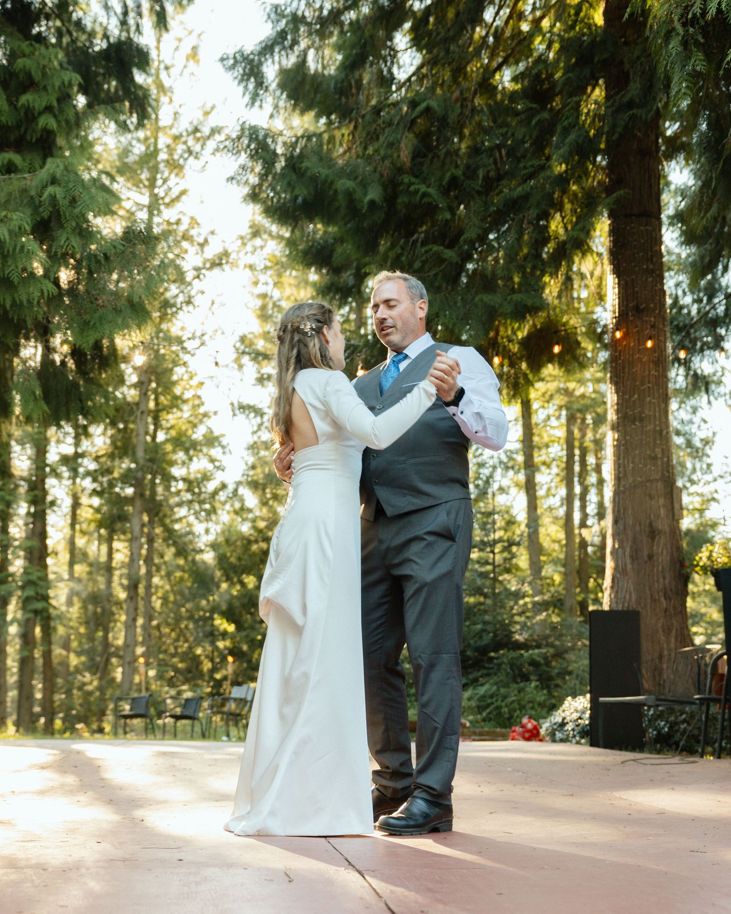 Emotional moment during father-daughter dance at a wedding reception. They are surrounded by tall beautiful trees and string lights.