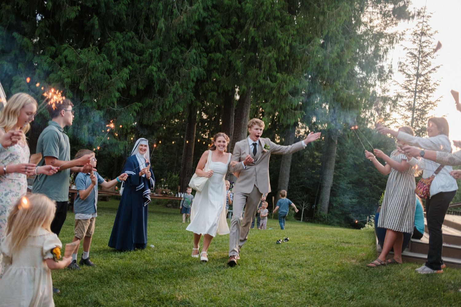 A bride and groom run through a sparkler send-off at their forest wedding, surrounded by cheering guests in a magical, joyful moment.