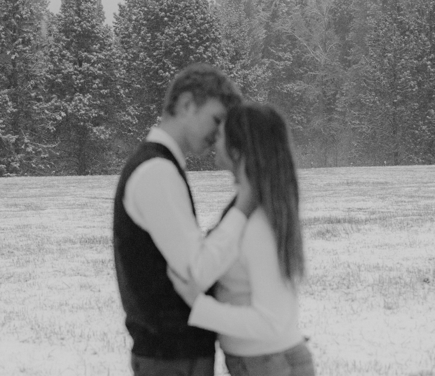 Romantic winter couple embrace captured in a snowy field, surrounded by frosted trees—timeless love in nature's serene, chilly beauty.