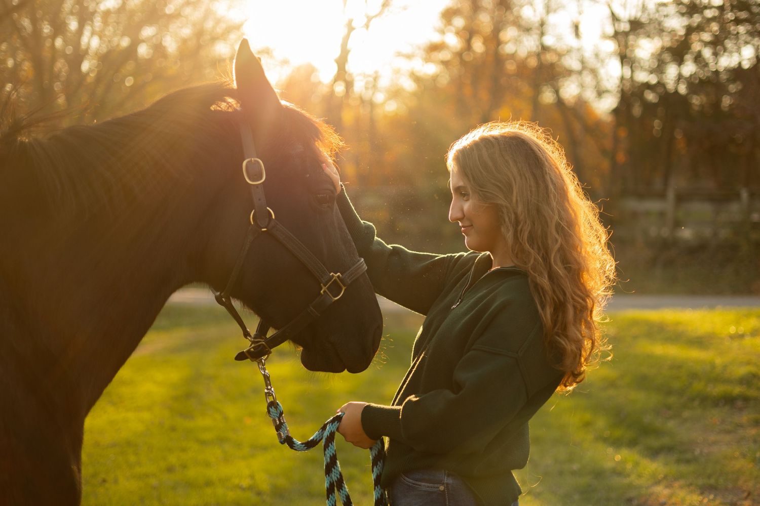Senior photo of a beautiful young woman bonding with her horse in golden sunset light.