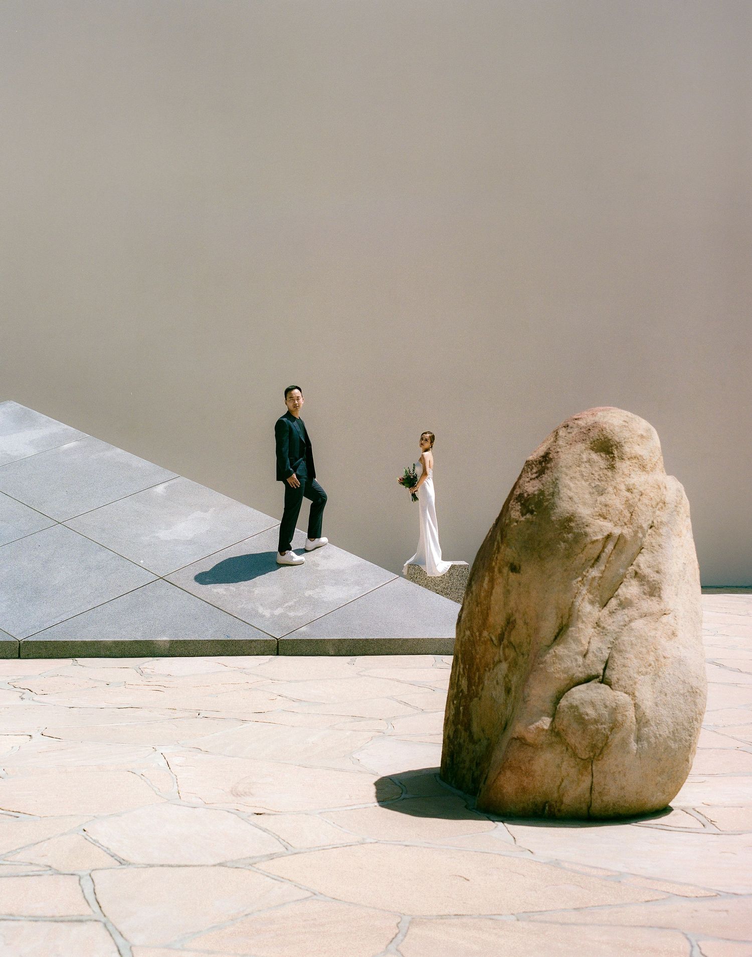 A minimalist wedding photo with a large rock formation and geometric stone platform.