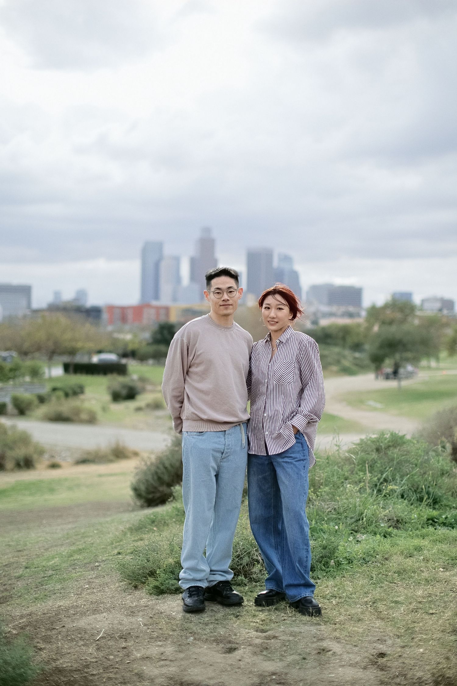 Casual couple portrait with downtown skyline backdrop on grassy hill.