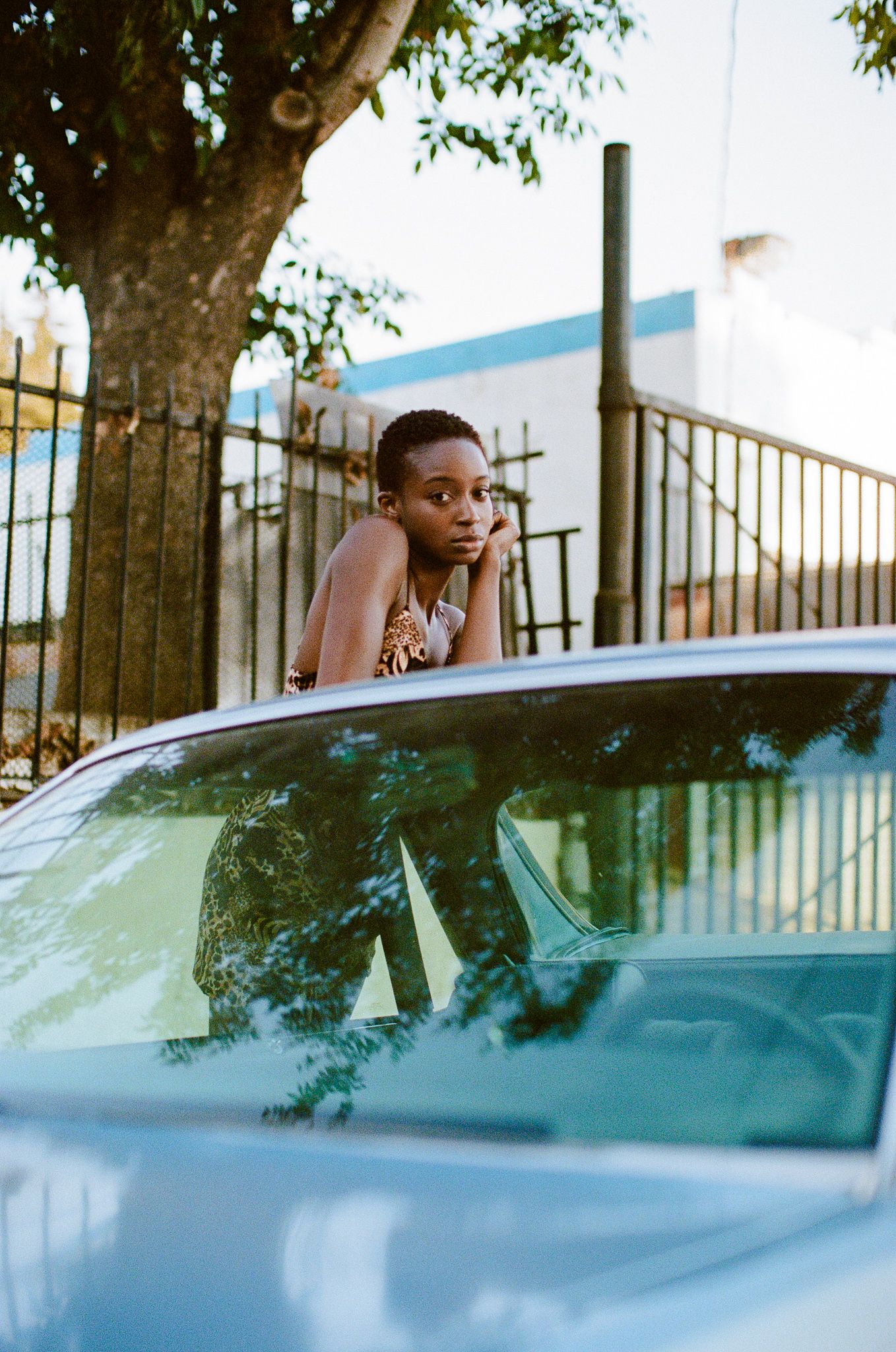 A stylish portrait with a leopard print dress against a vintage blue car on a sunny day.