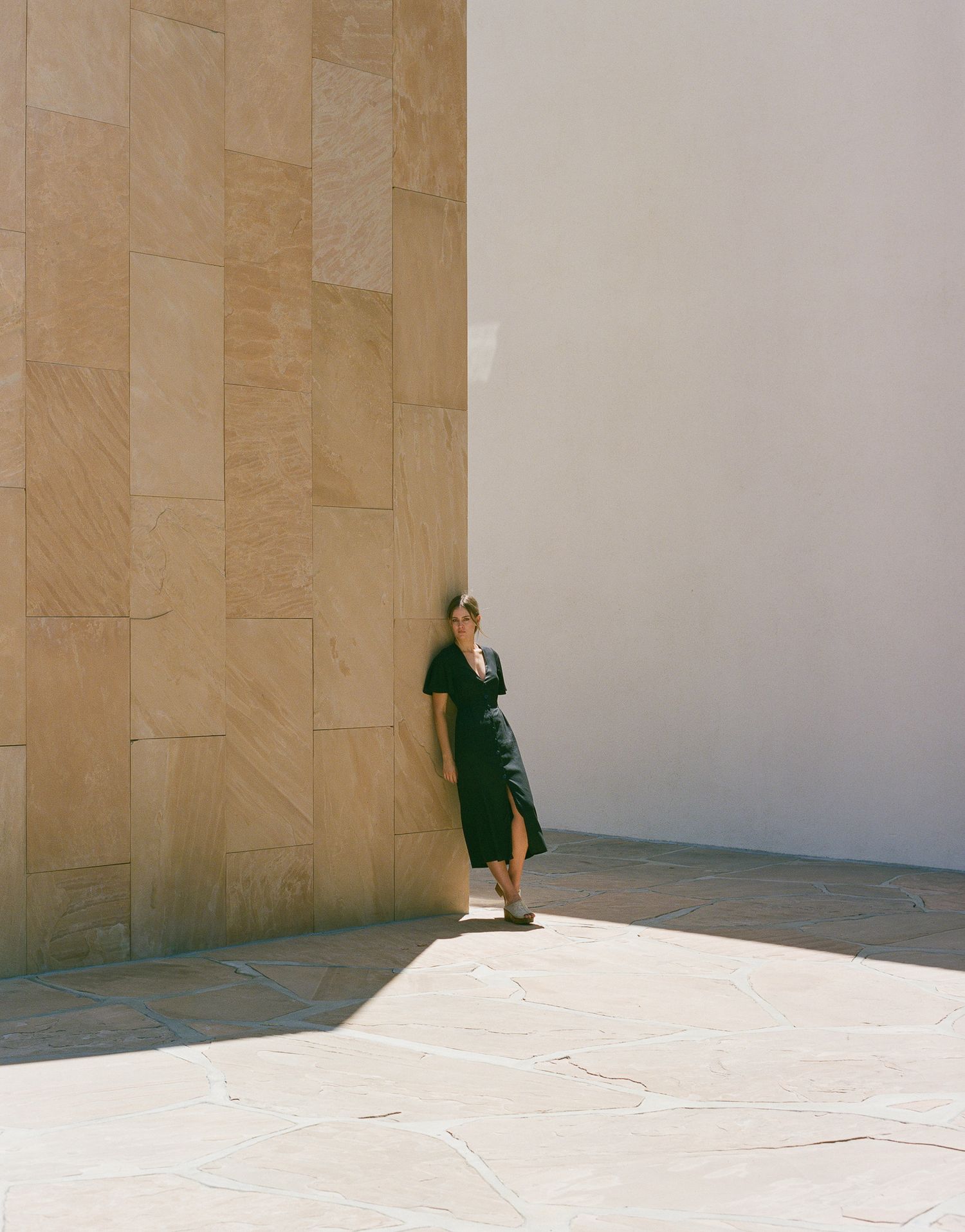 A minimalist fashion photo featuring a dark green dress against beige stone walls.