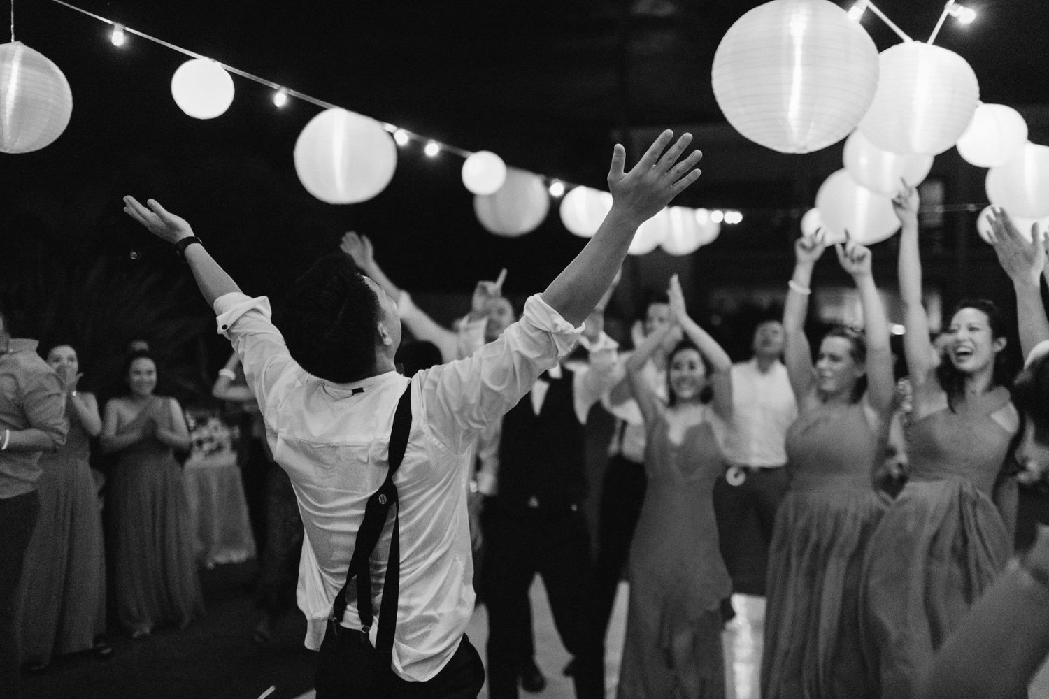 Black and white photo of wedding celebration with paper lanterns and dancing under night sky.