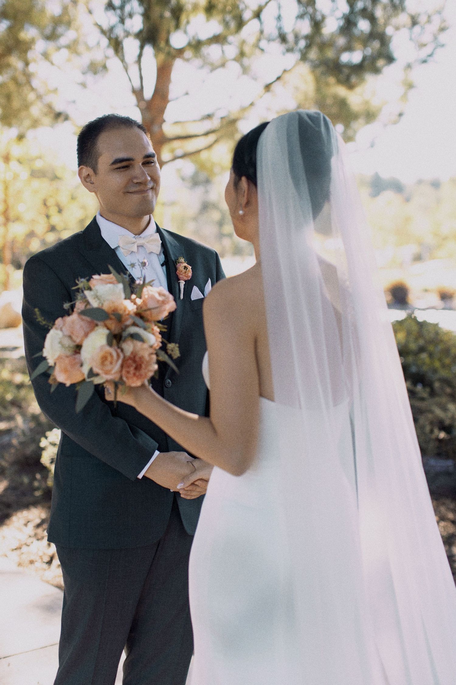 A tender wedding moment with the groom holding a bouquet of peach roses.