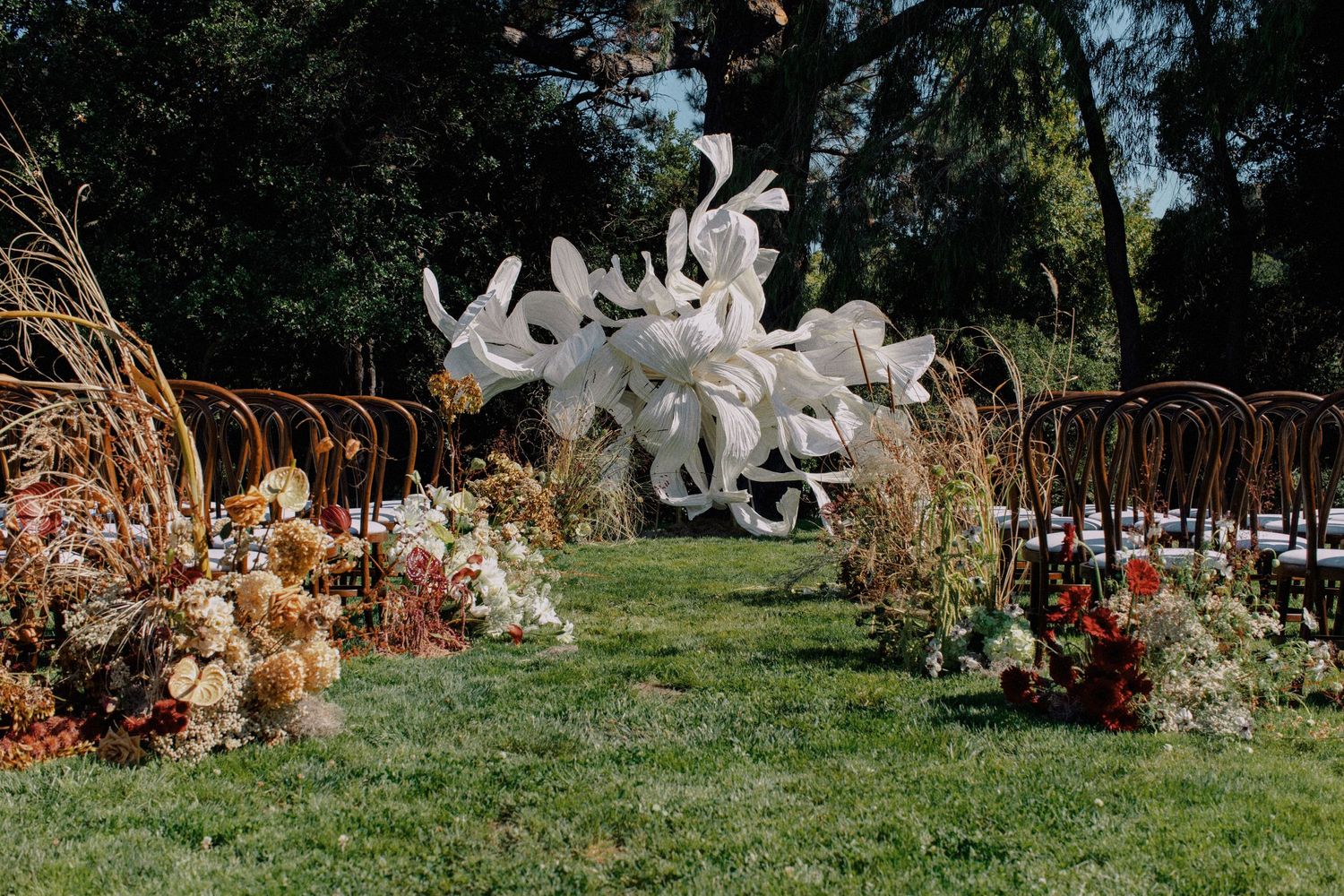Outdoor wedding ceremony setup with white floral installation and wooden chairs.