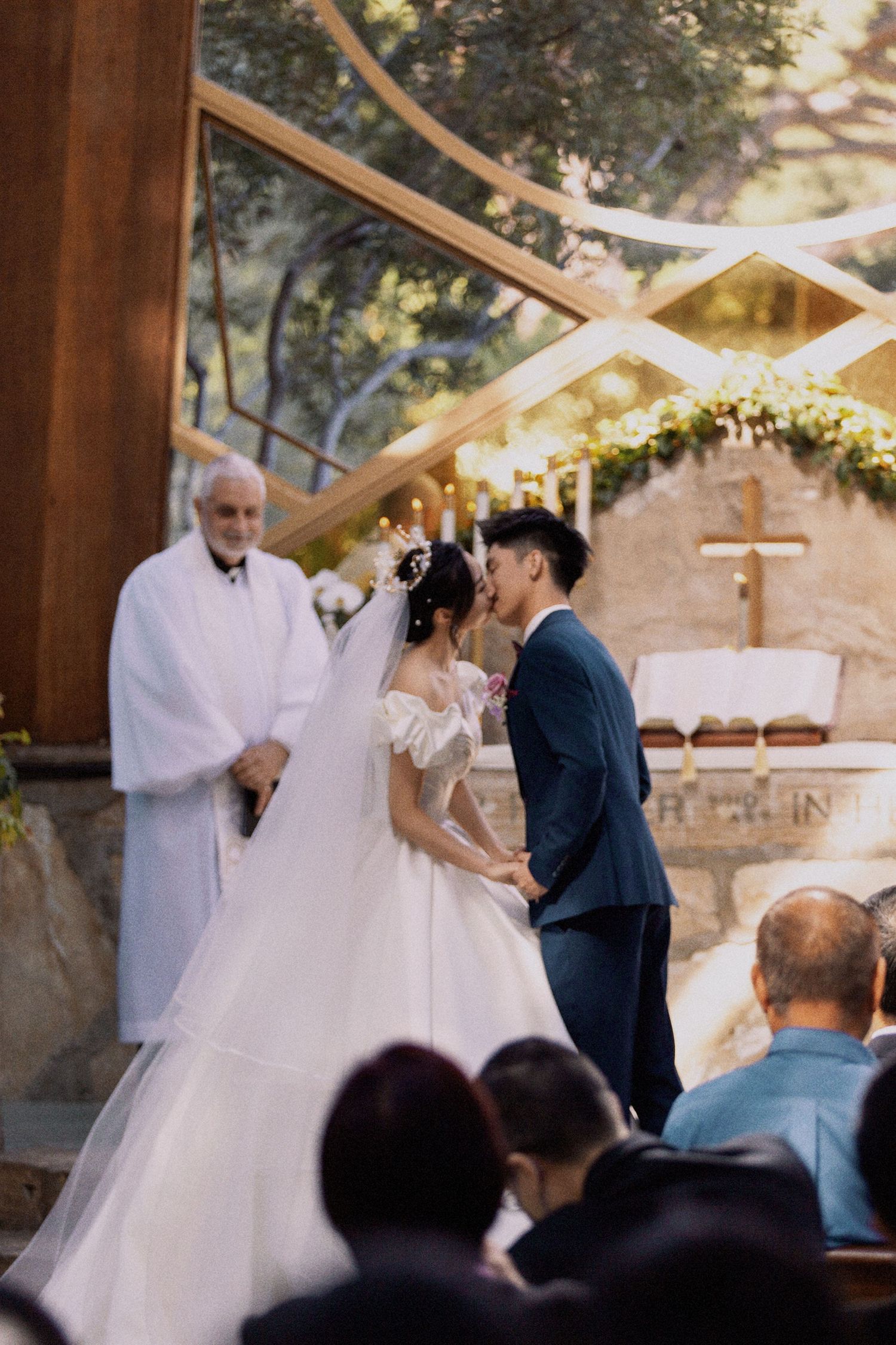 A wedding ceremony in progress at an outdoor chapel with wooden beams and floral decorations.