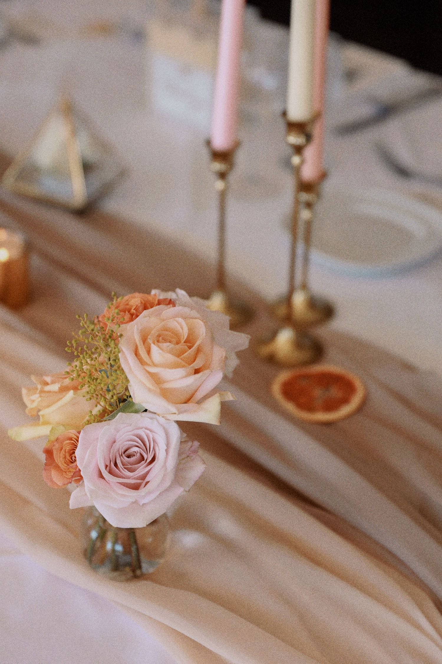 Soft pink roses and peach candles create an elegant table setting with golden candlesticks.