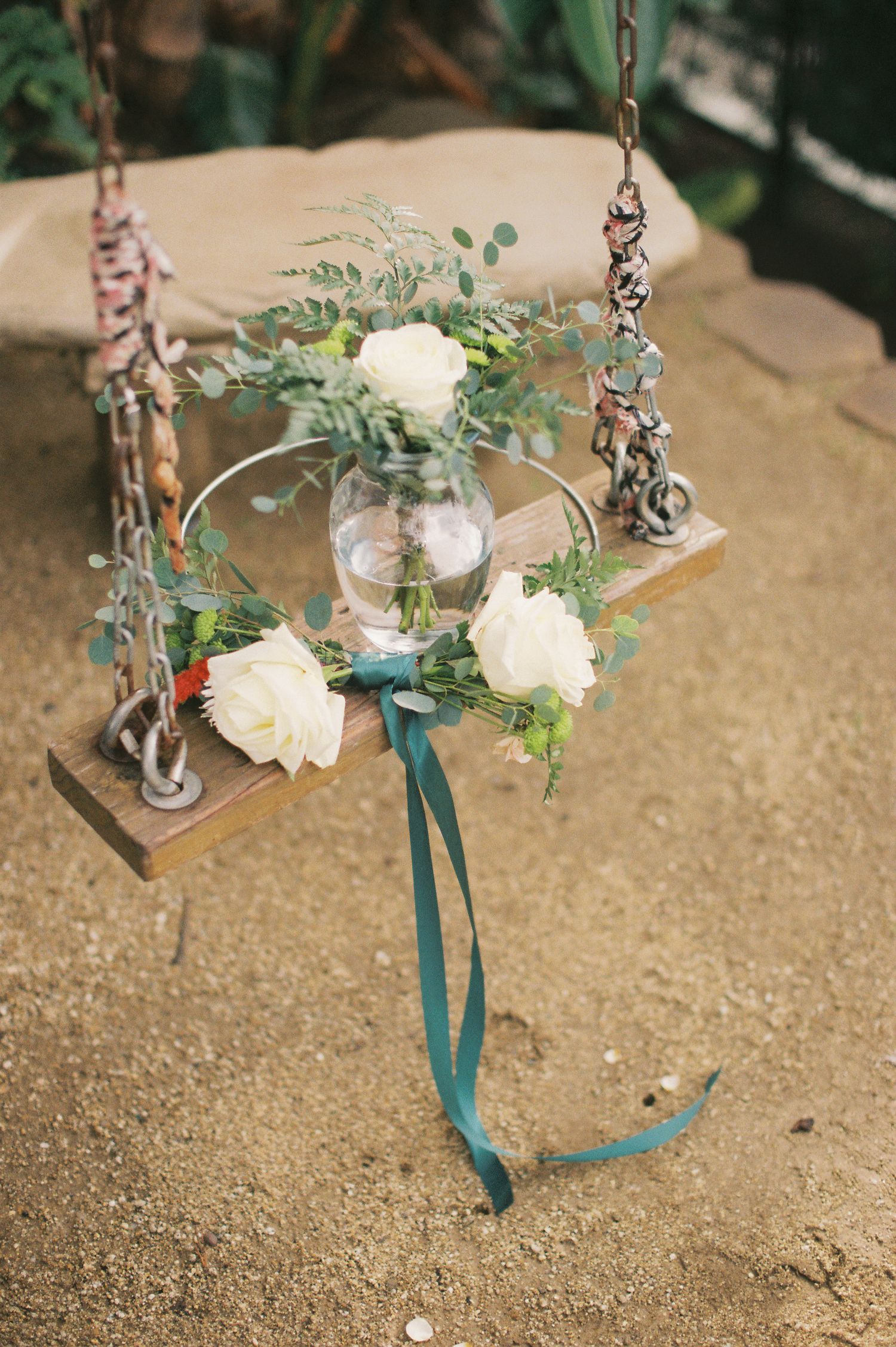 Rustic wooden swing decorated with white roses and eucalyptus in a garden setting.
