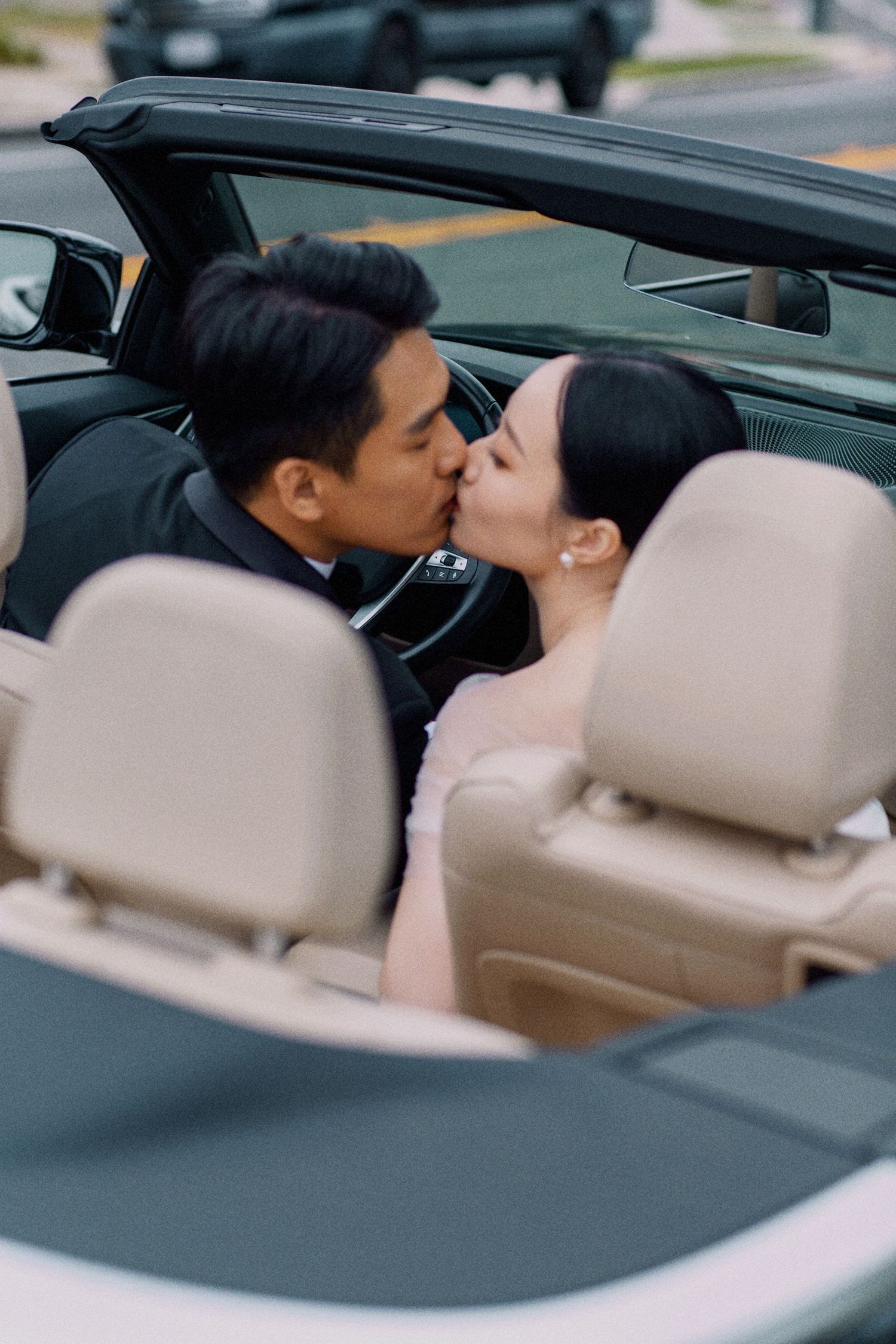 A romantic couple sharing a kiss in a convertible car with beige leather seats.