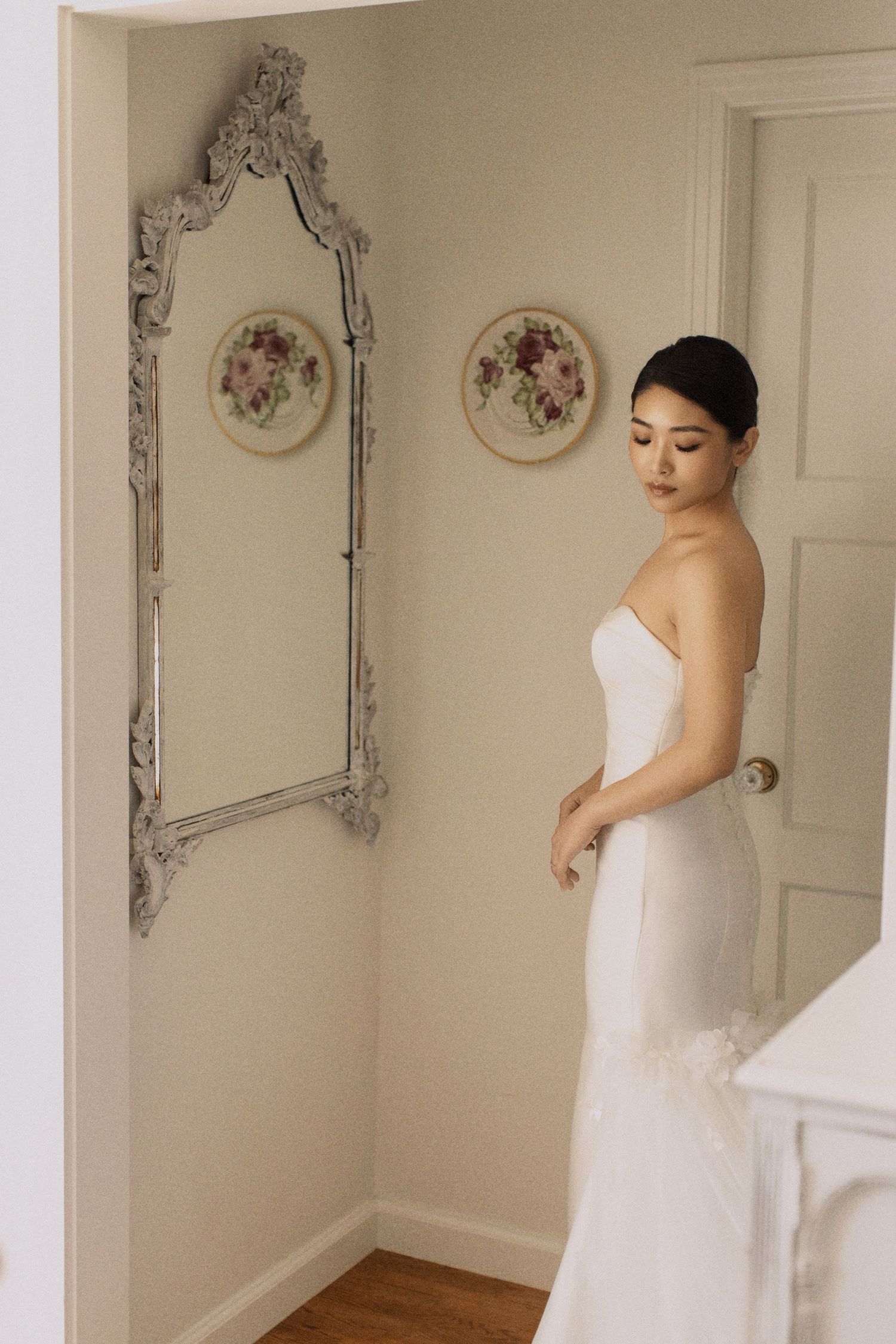 Elegant white gown shown in ornate mirror reflection with decorative plates on wall.