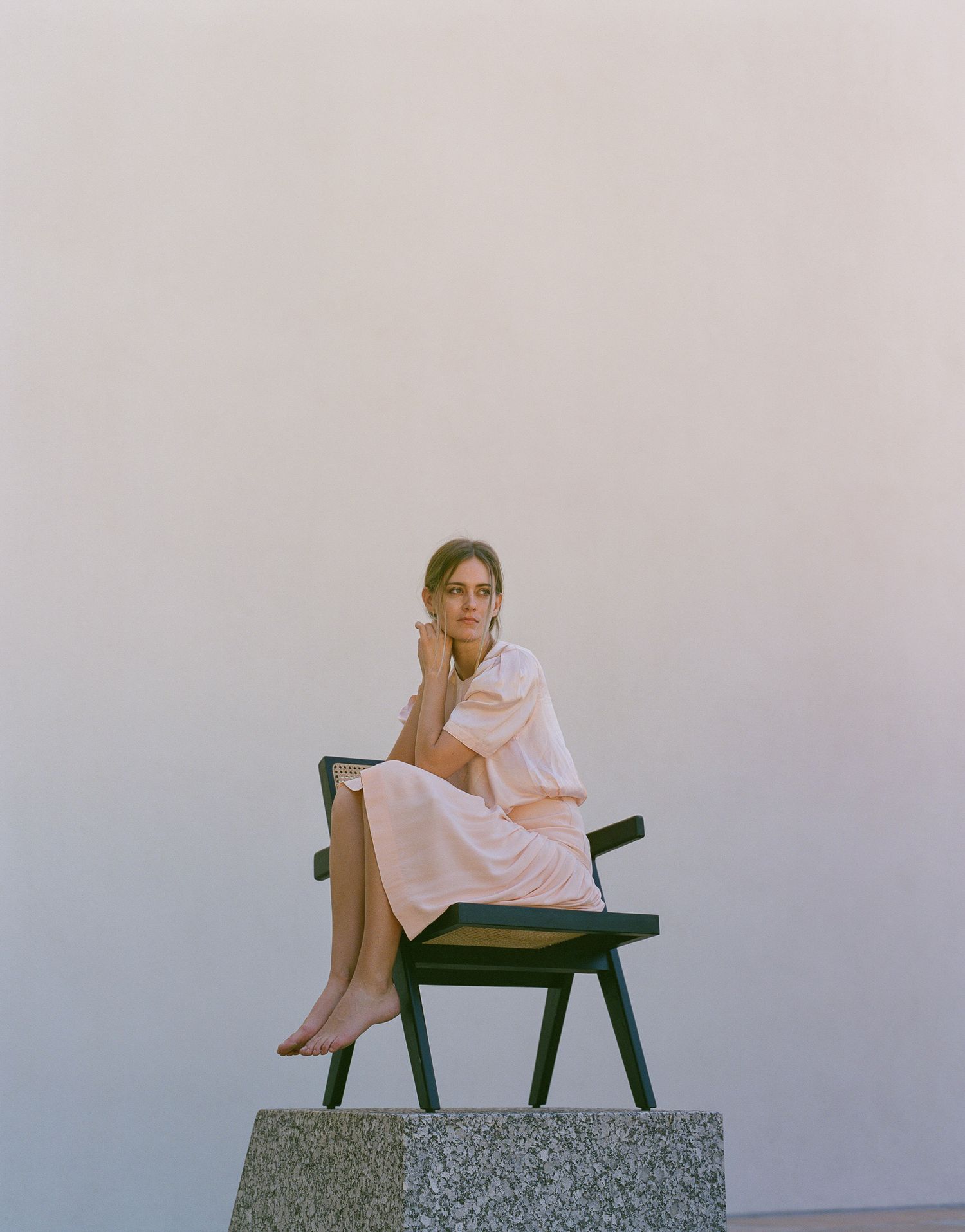 A figure in a pink dress sits pensively on a green bench atop a concrete platform.
