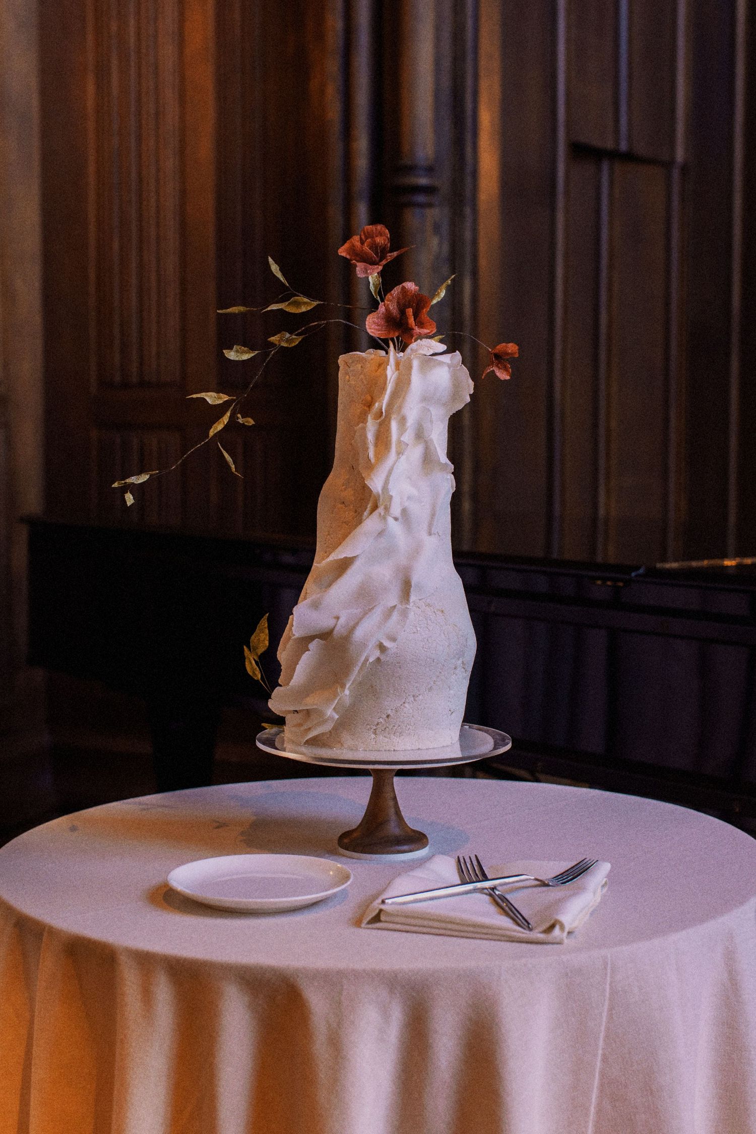 Modern white wedding cake with red floral accents on a round table.