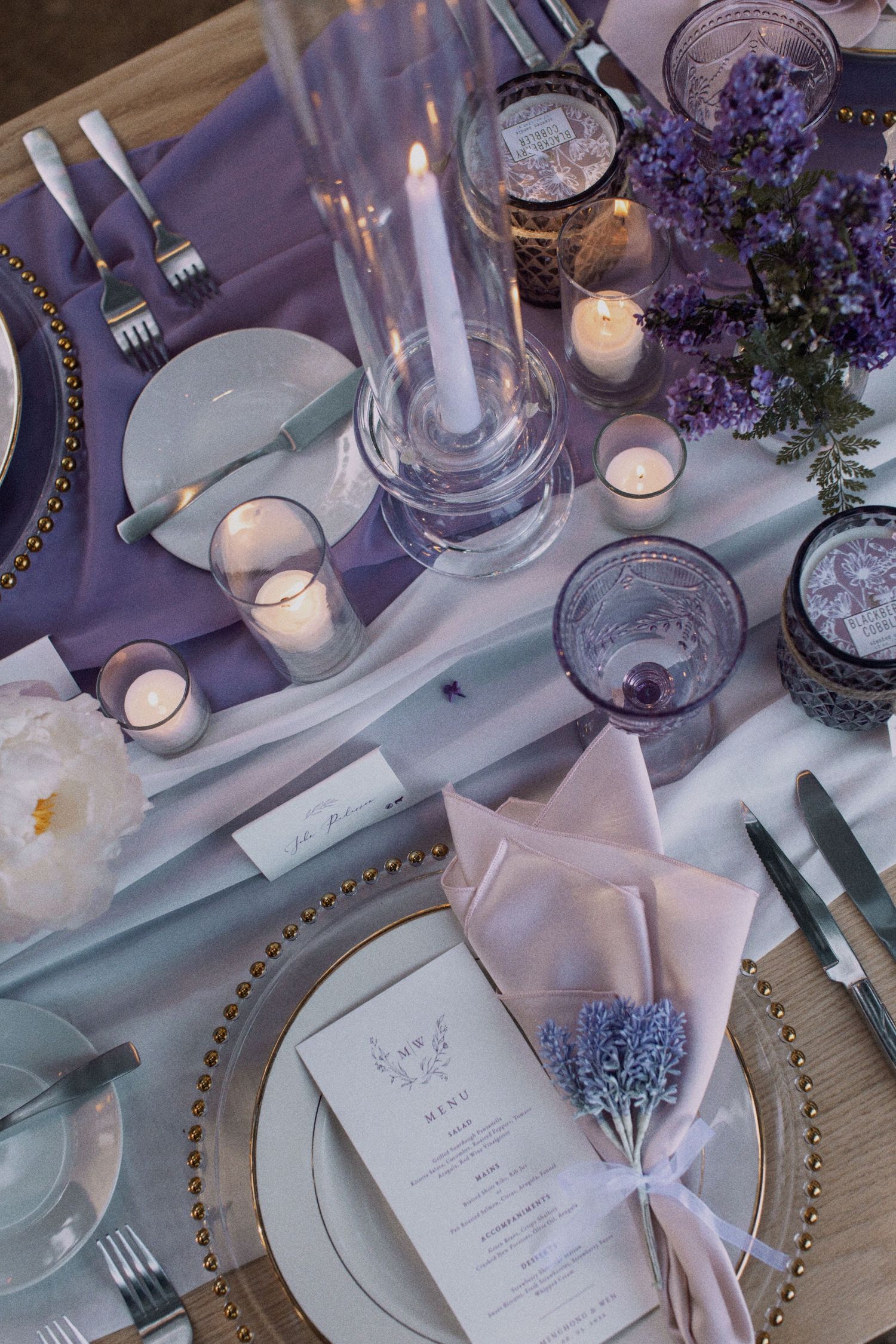 Purple and white table setting with crystal glasses, candles and elegant place cards.