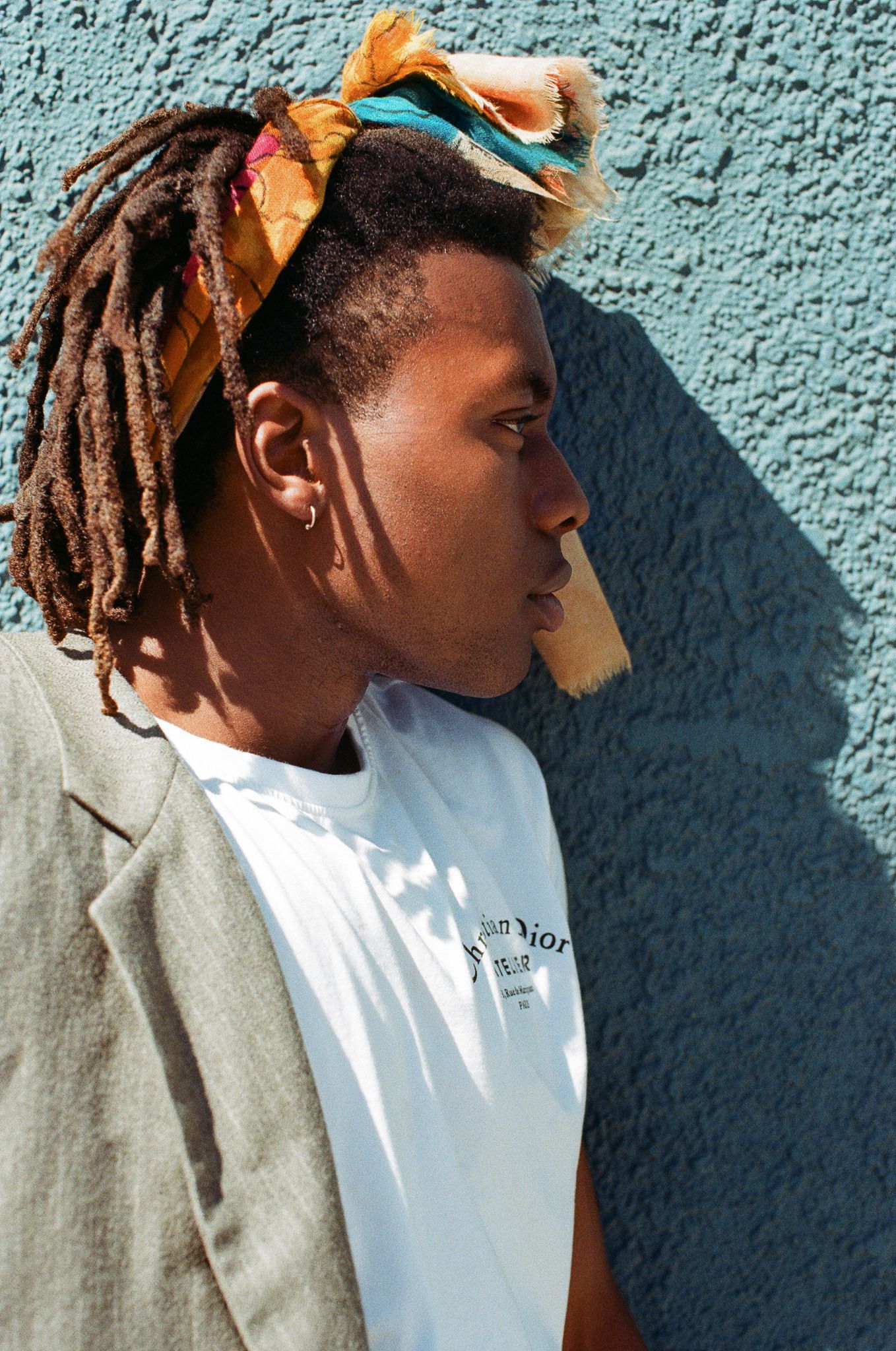 Profile view of person wearing orange headscarf and white t-shirt against turquoise wall.