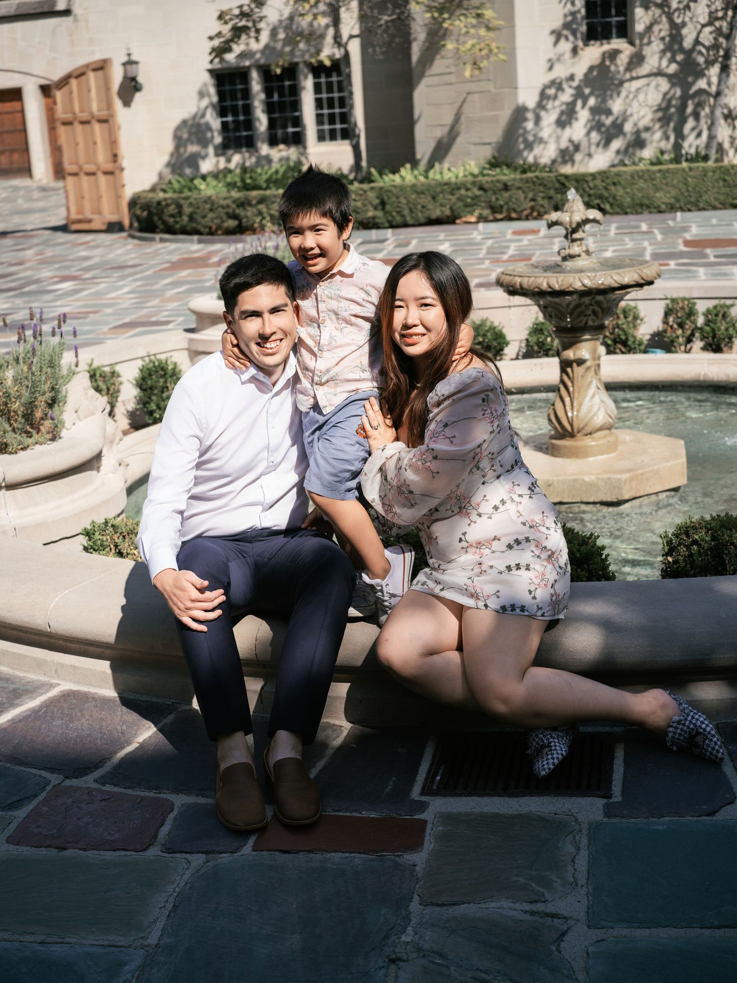 Happy family sitting together on stone ledge by fountain in courtyard.