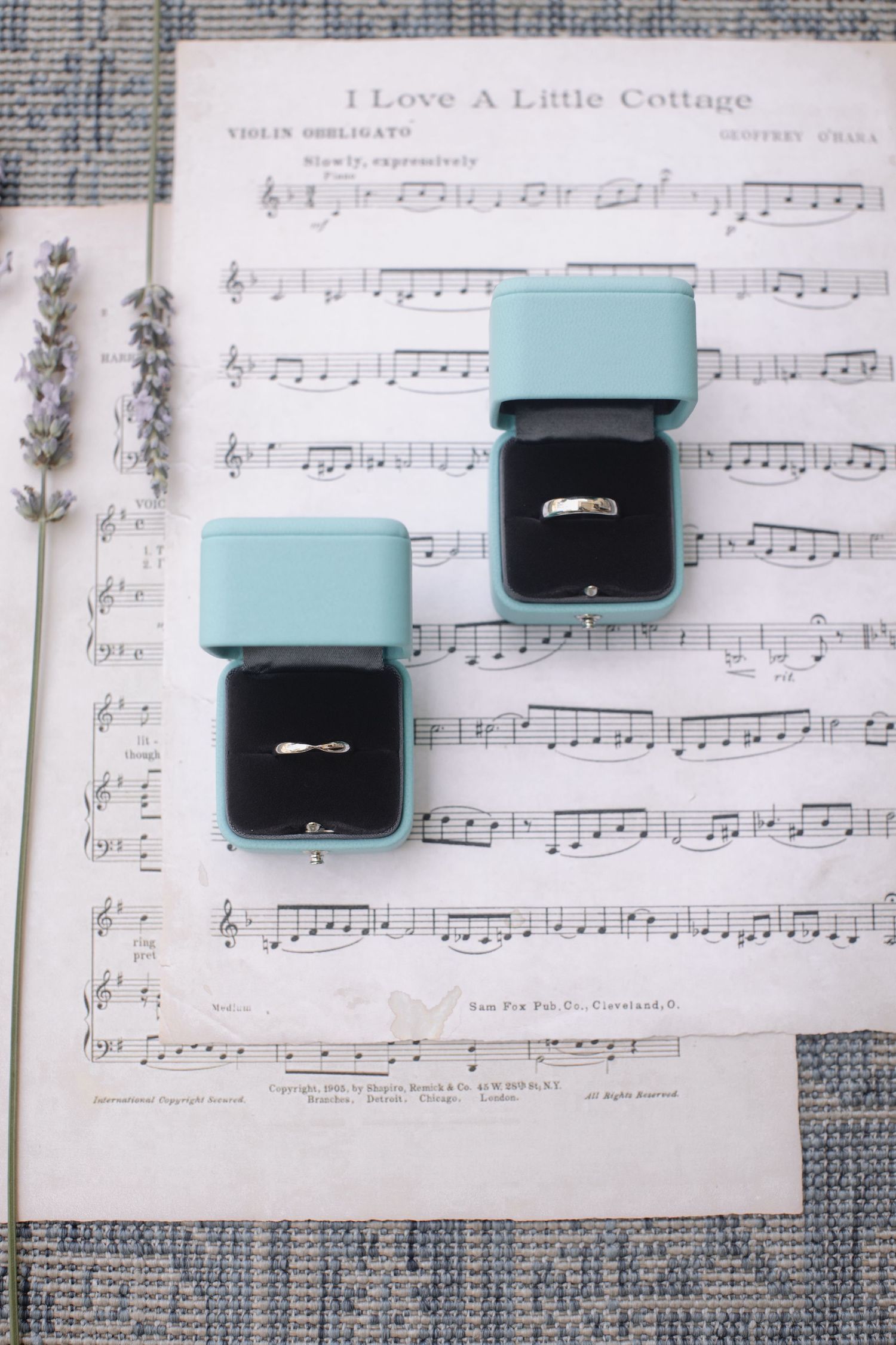 Two teal ring boxes displaying engagement rings placed on vintage sheet music.
