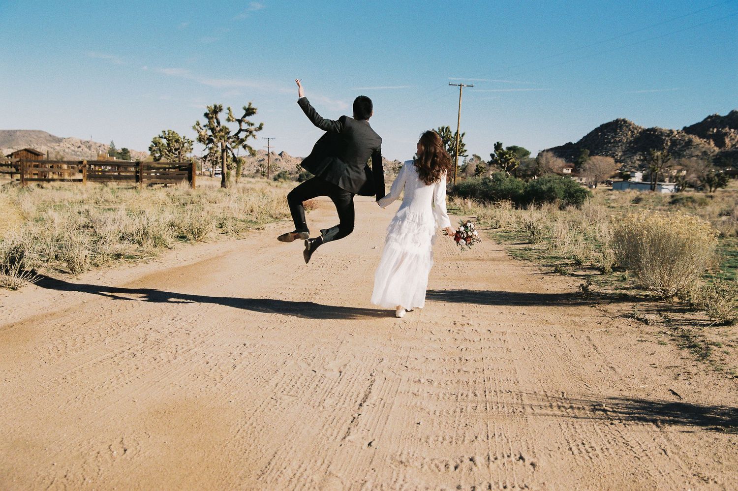 Joyful couple celebrating on a dirt road in the desert, with one person leaping into the air.