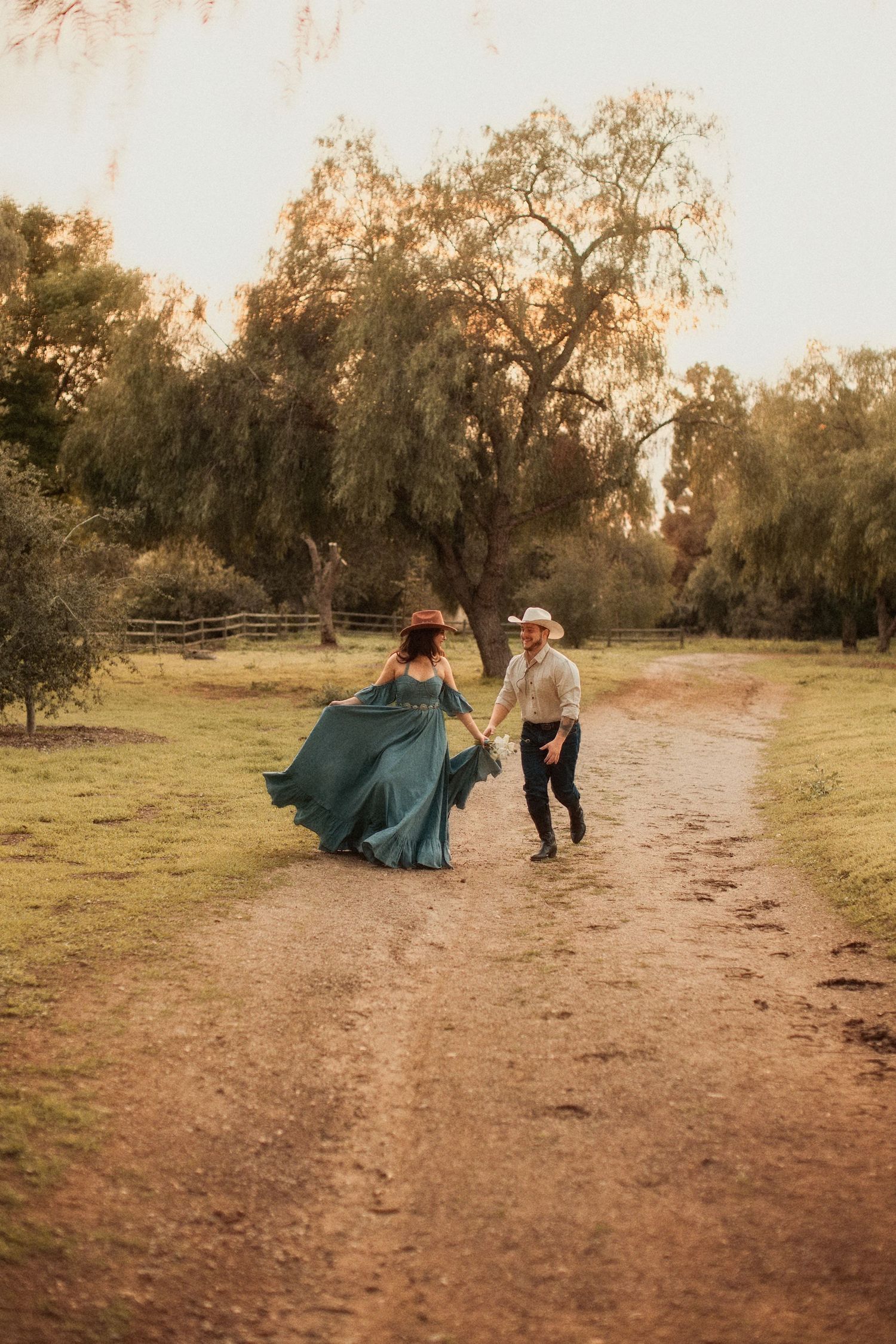 A couple dances together on a dirt path surrounded by willow trees at sunset.