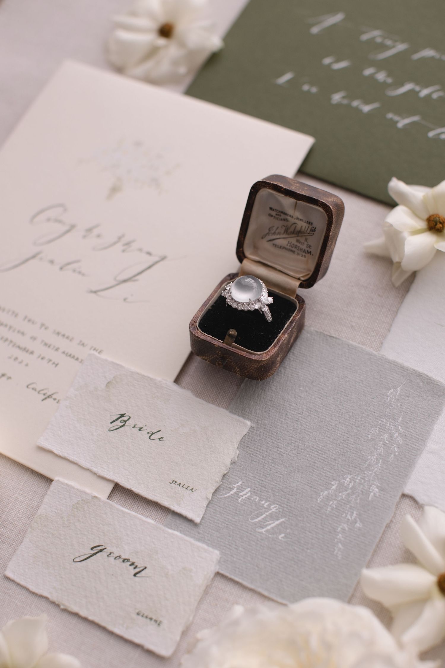 Vintage-style engagement ring in brown velvet box with wedding stationery and white flowers.