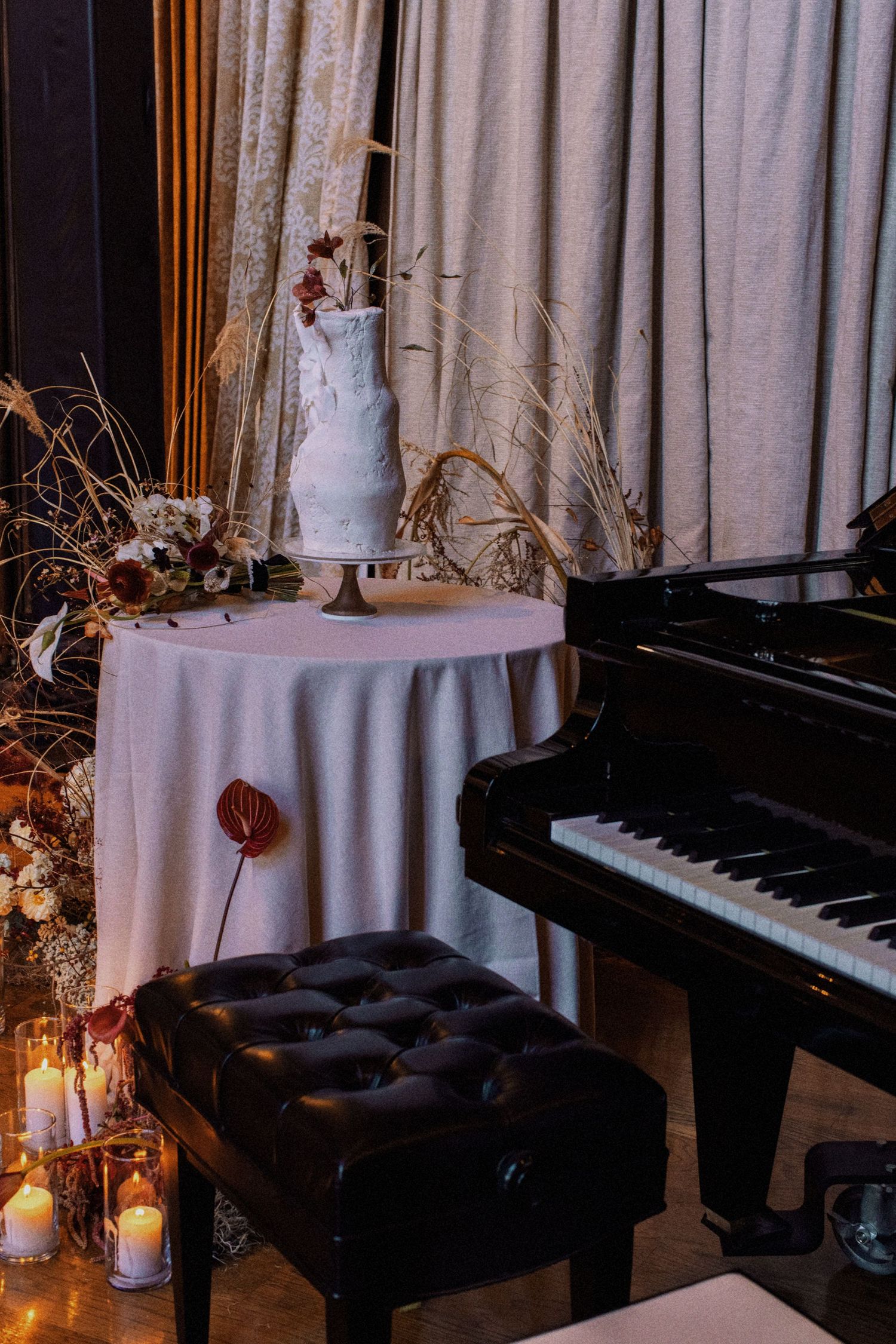 Wedding reception decor featuring a piano, tiered white cake, and romantic candlelight.