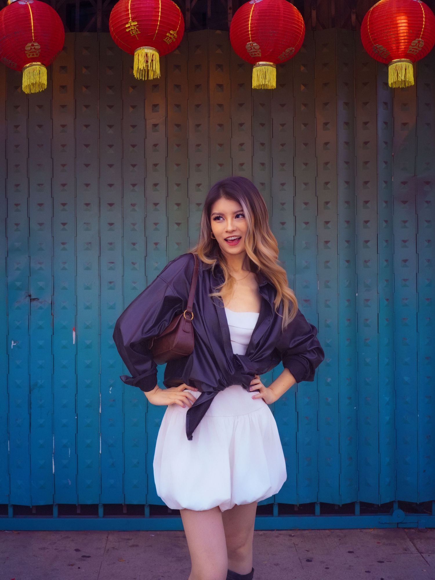 Model in white dress poses against blue wall with red Chinese lanterns.