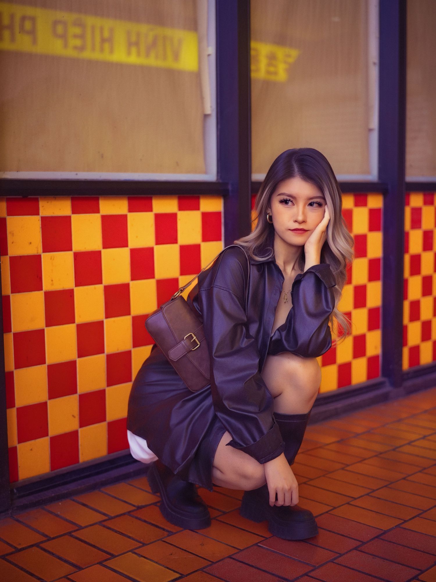 Fashion model crouches in black outfit against retro checkerboard wall.