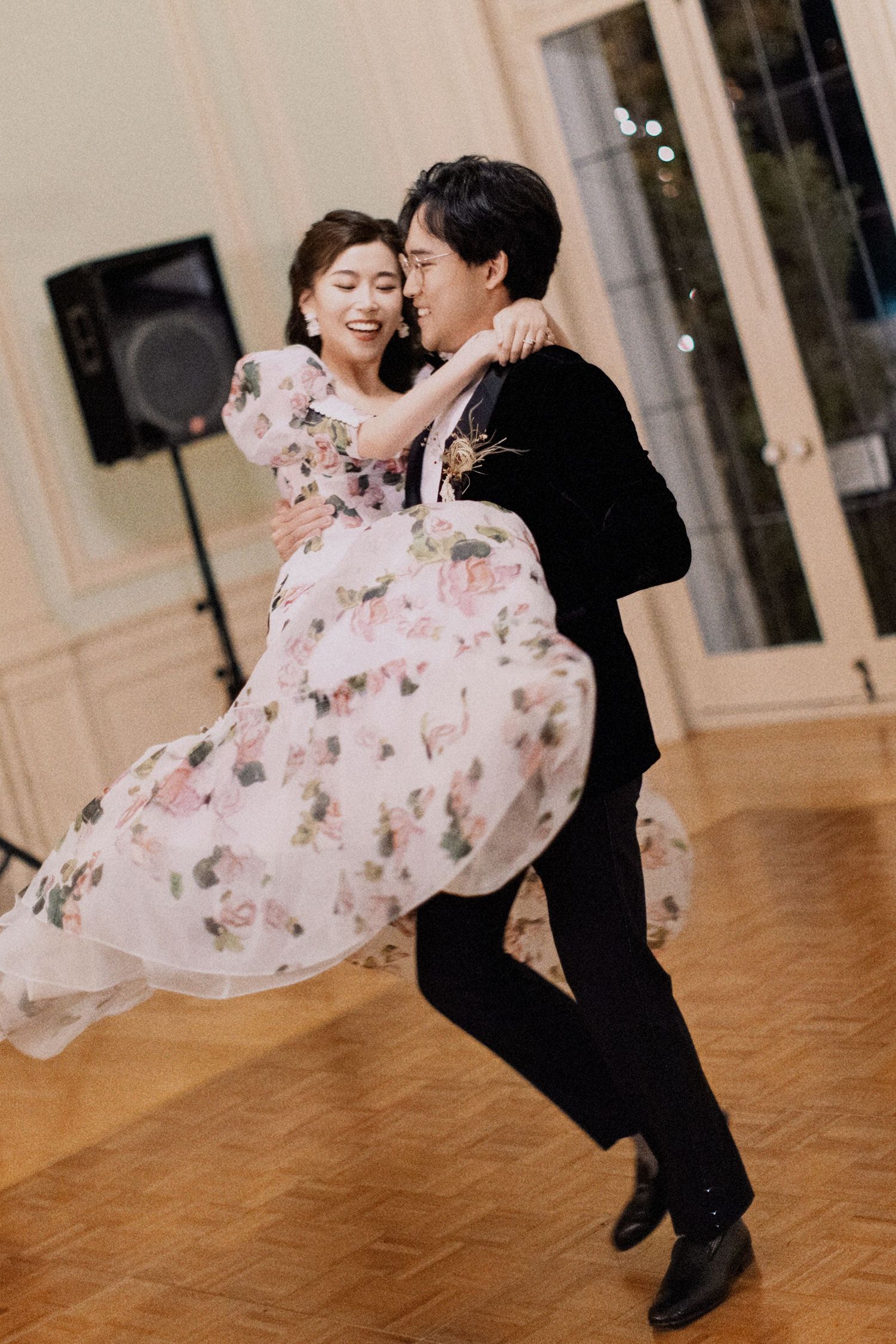 A couple dances elegantly at their wedding, with the bride wearing a flowing floral dress and groom in black.