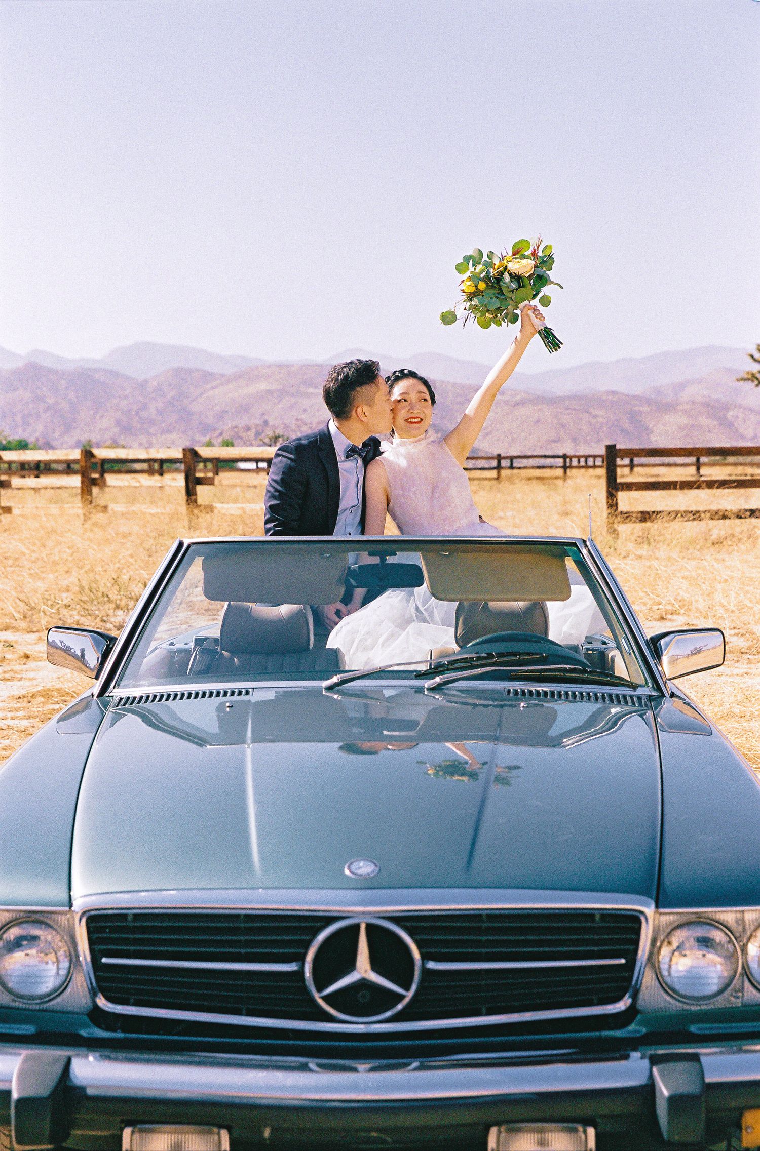 A joyful wedding couple in a vintage Mercedes convertible celebrating with a bouquet toss.