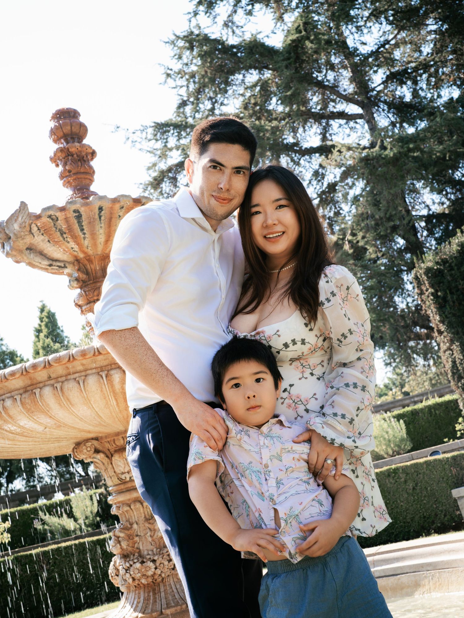 A family poses together in front of an ornate stone fountain in a garden setting.