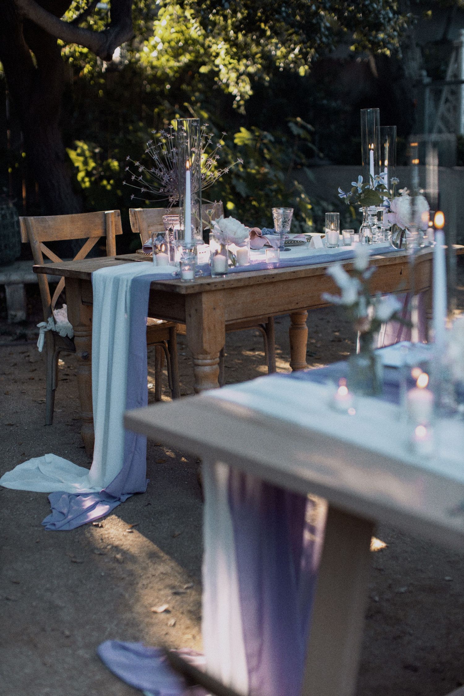 Rustic wedding reception table with blue runners and candles in an outdoor garden setting.