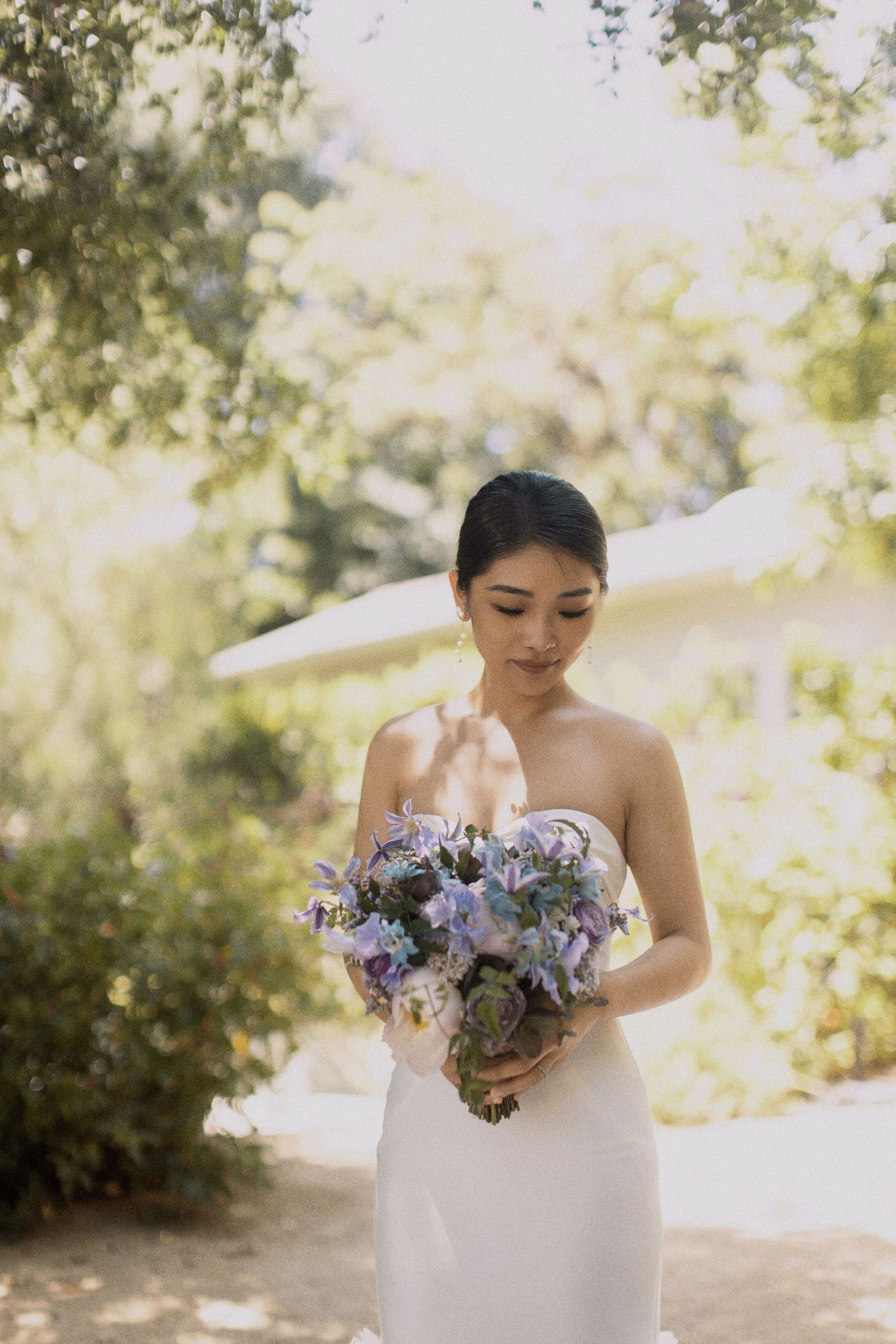 Beautiful purple and lavender wedding bouquet held against white dress.