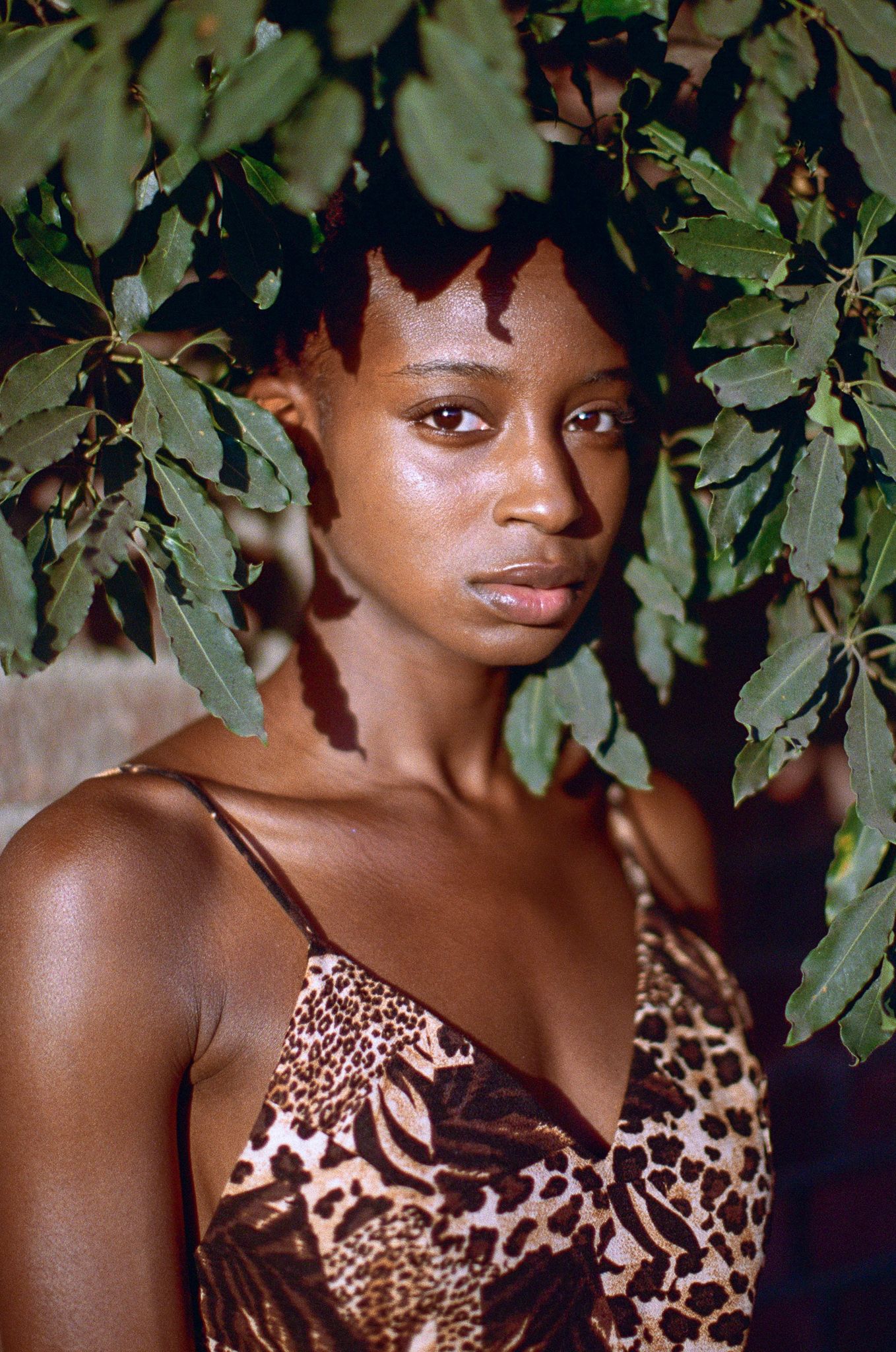 Portrait under green foliage wearing a brown and beige patterned dress.