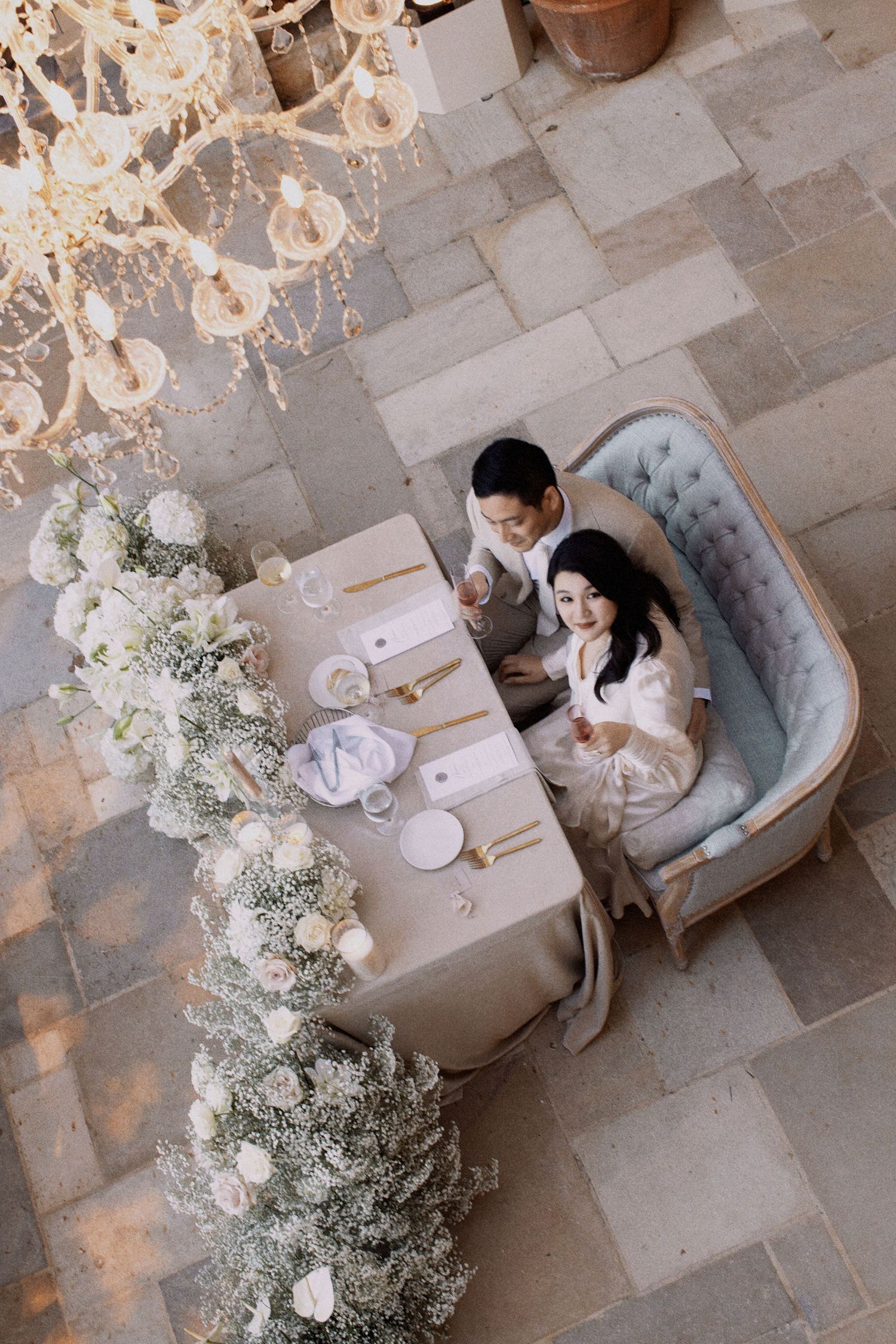 Overhead view of elegant white floral wedding reception setup with couple at table.
