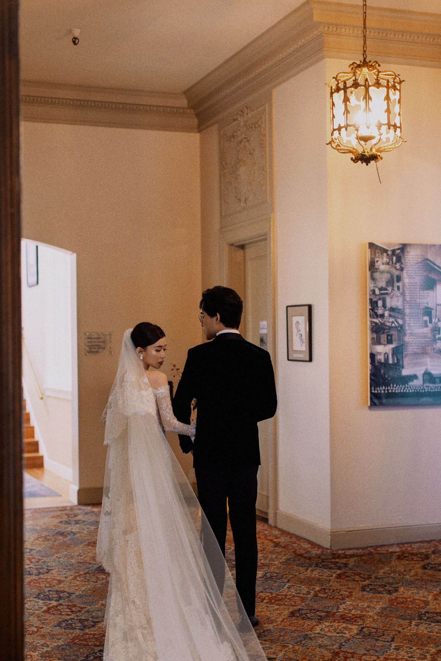 A wedding couple walking down an elegant hallway with a vintage chandelier.