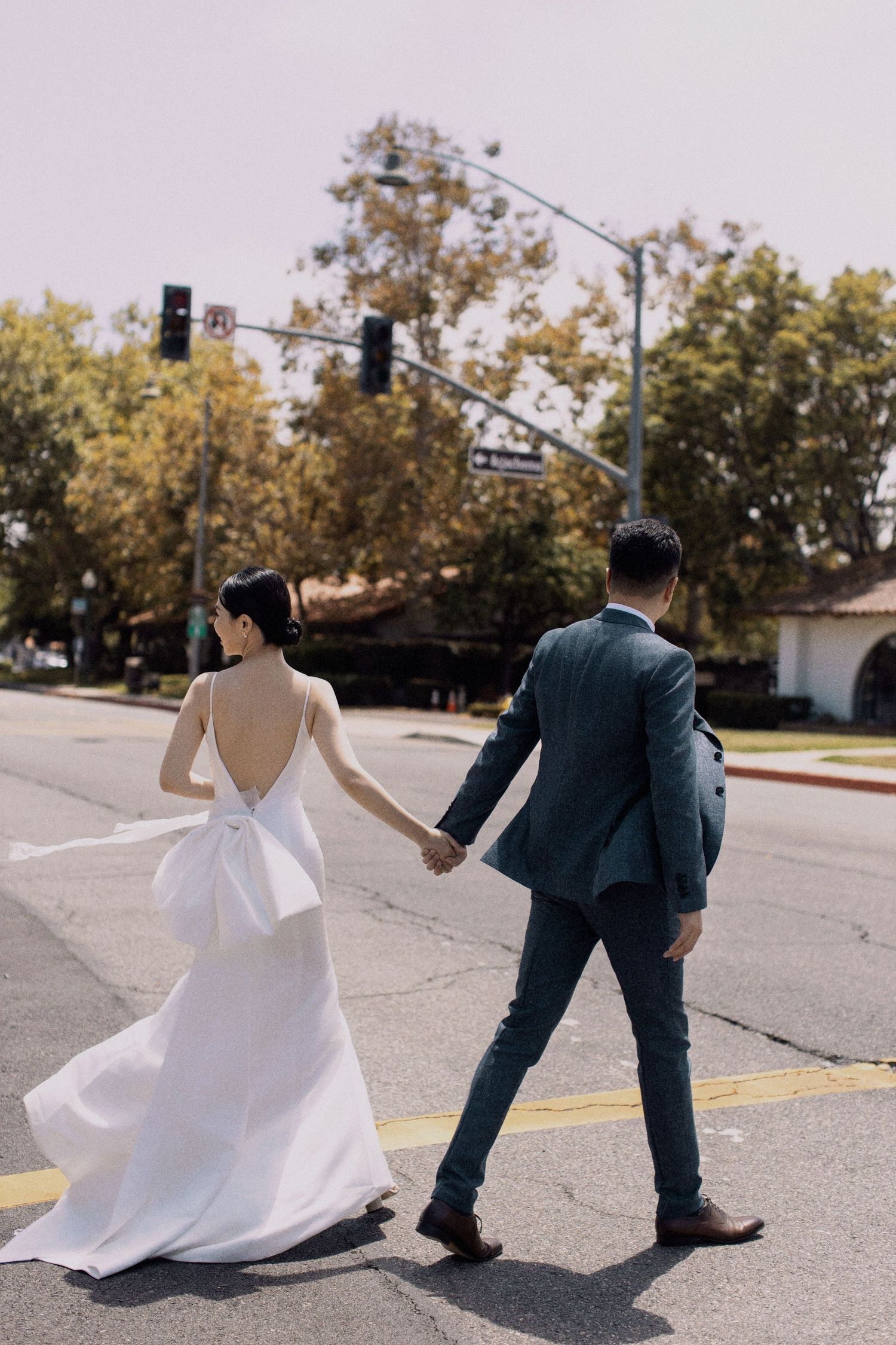 Couple walking hand in hand across street, bride in flowing white dress.