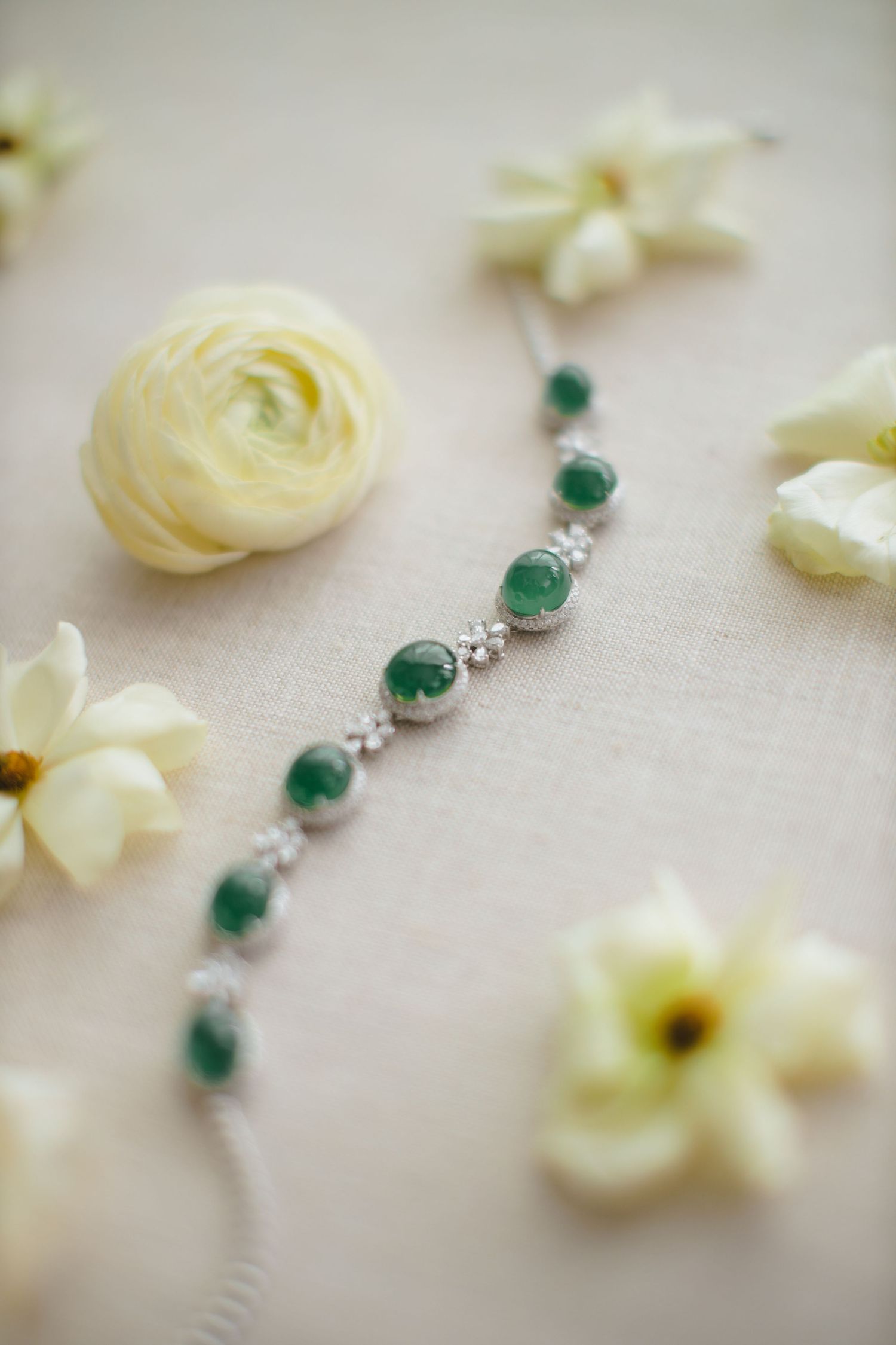 Delicate emerald and silver bracelet surrounded by cream colored flowers.