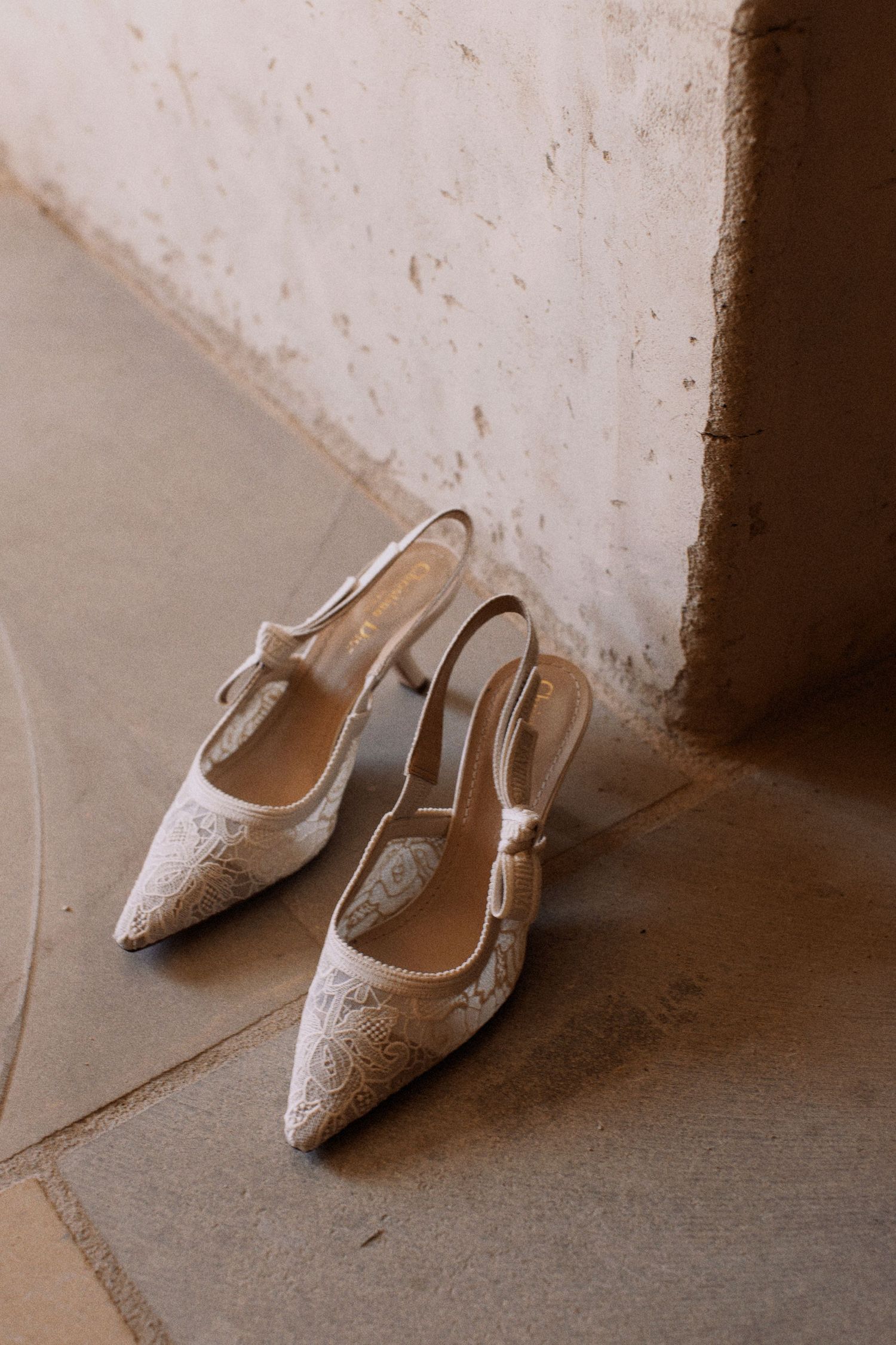 Elegant white lace bridal slingback heels on a textured beige floor.