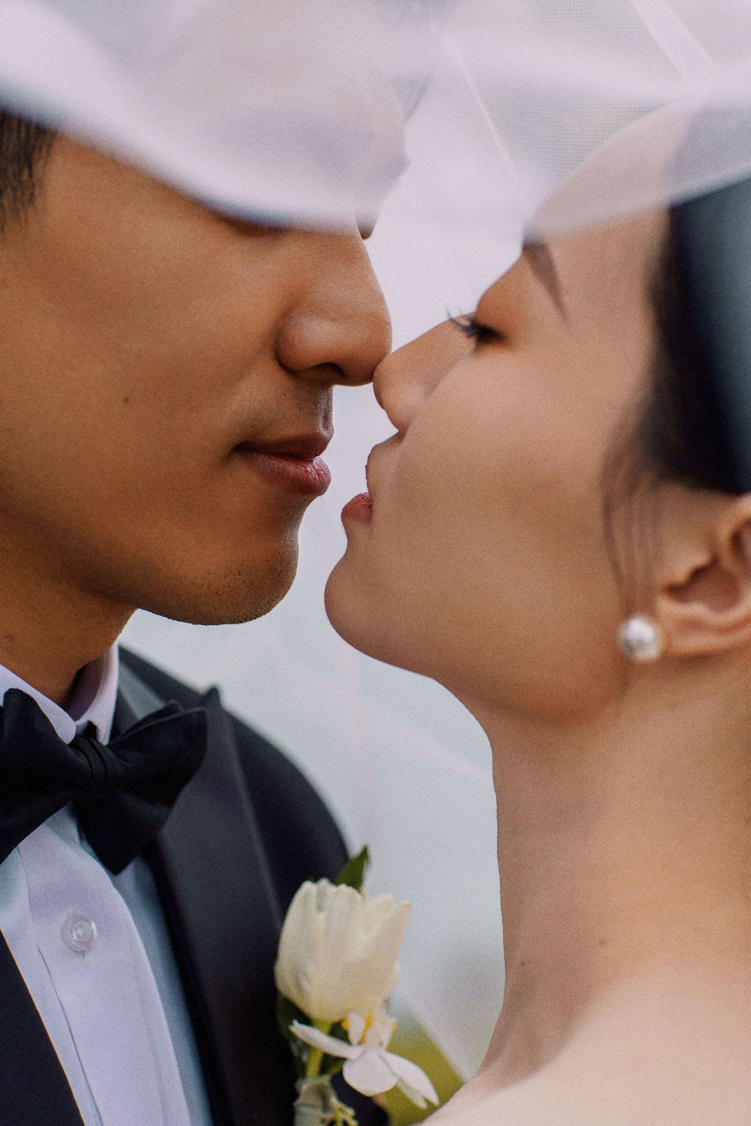 A close-up shot of newlyweds about to kiss, with the groom wearing a white boutonniere.