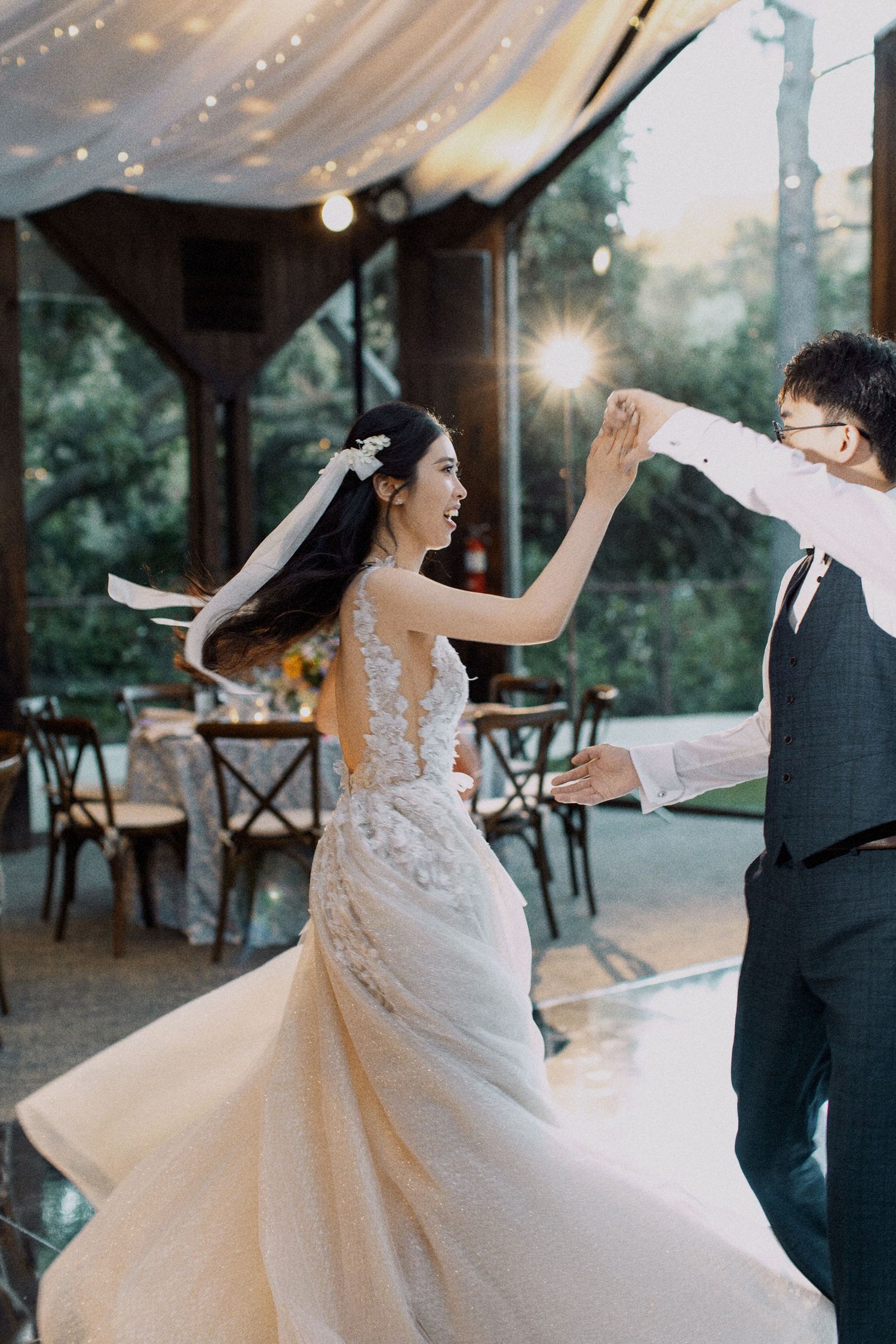 Joyful dancing moment at a wedding reception under string lights and tent covering.