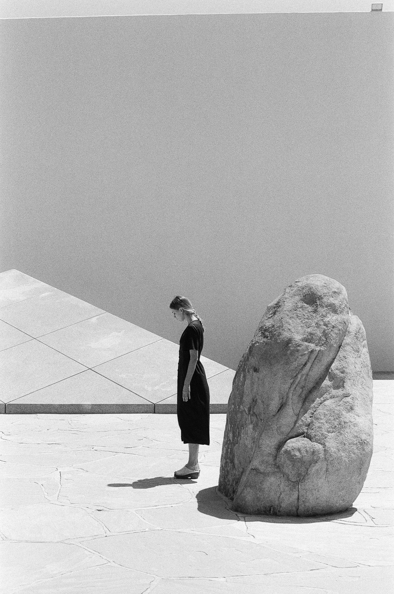 Minimalist black and white photo of figure standing next to large rock formation.
