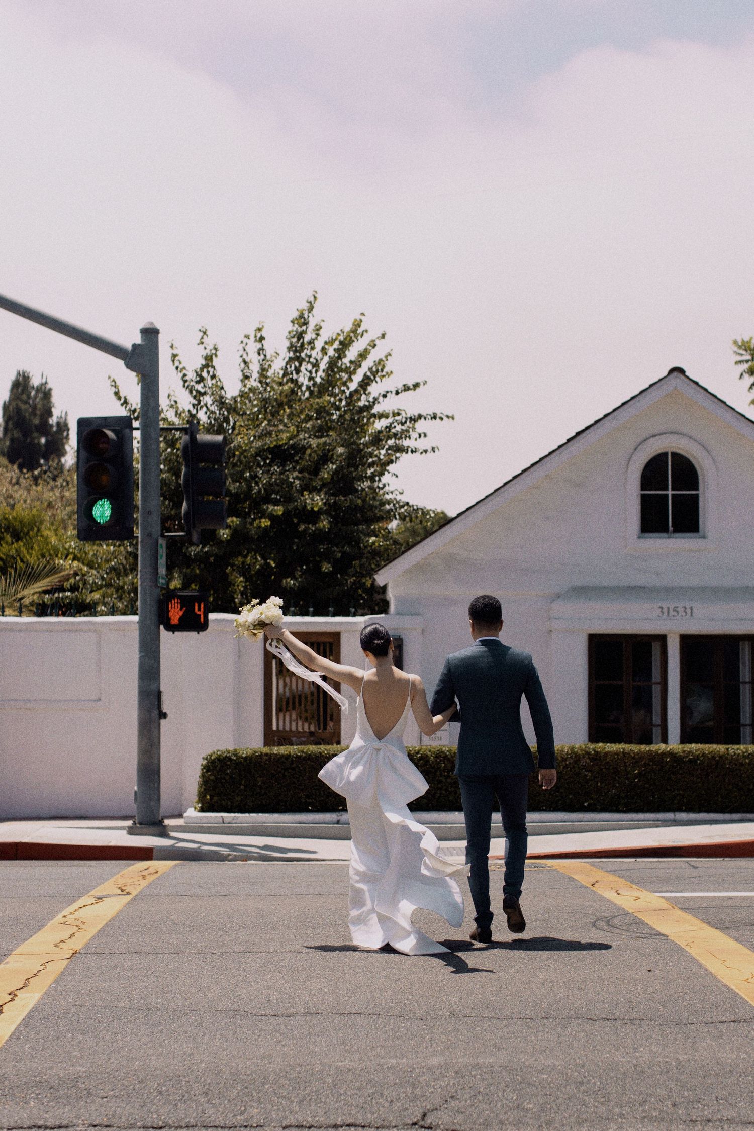 Newlywed couple walking away on crosswalk towards white church building.