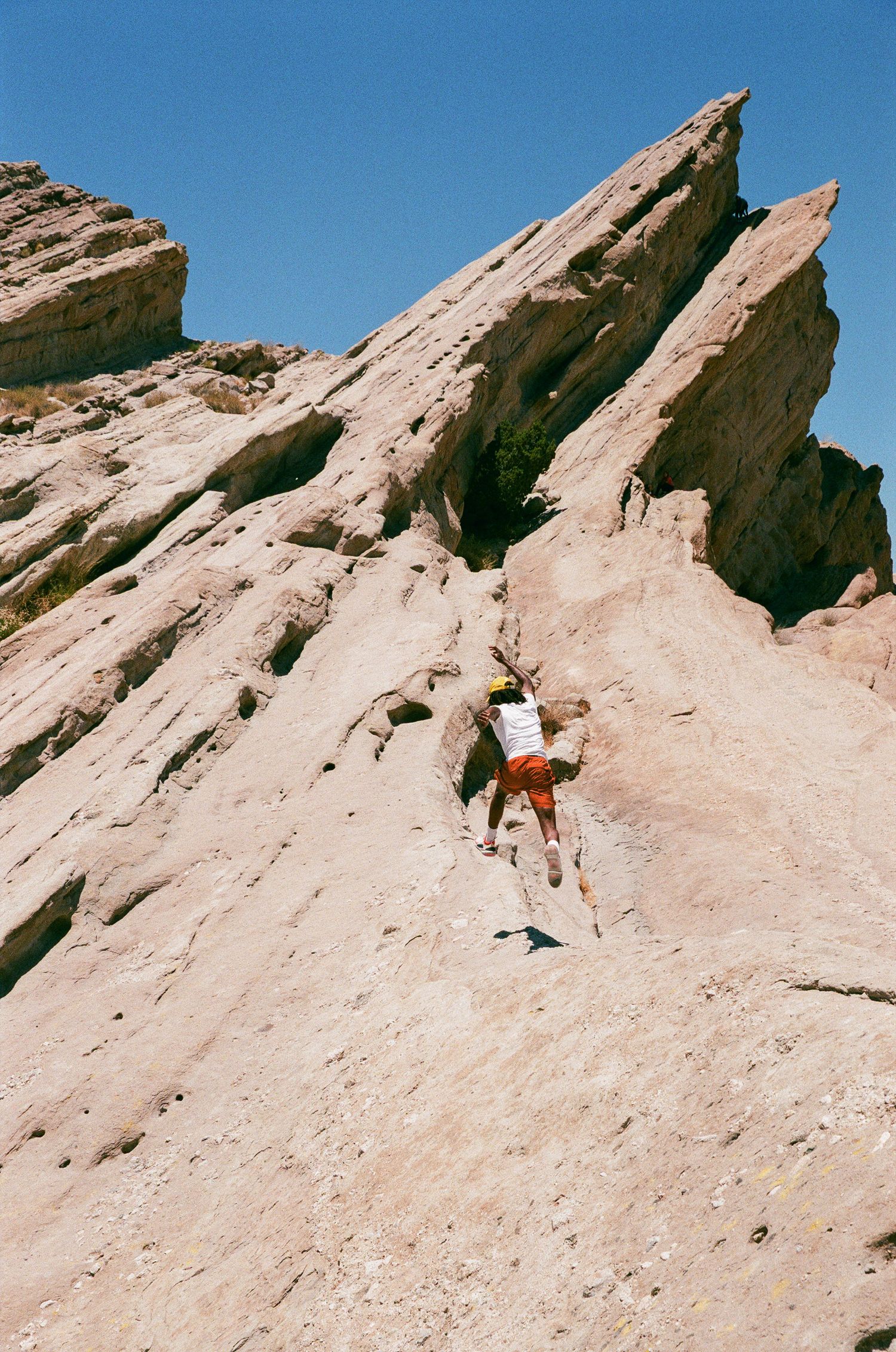 A climber scales a steep rocky cliff face in the desert landscape.