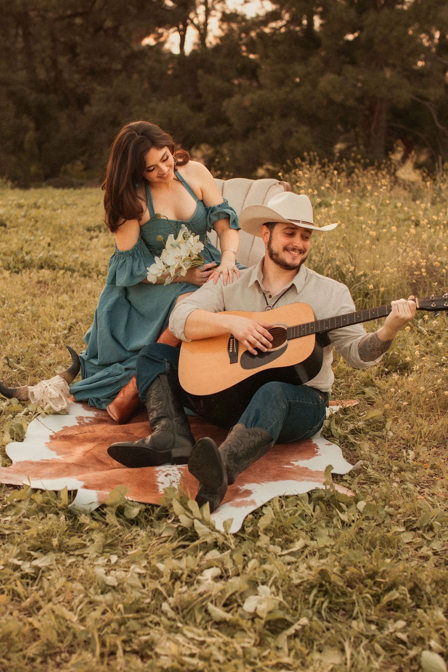 A couple shares a romantic moment on a blanket at sunset while playing acoustic guitar in a grassy meadow.