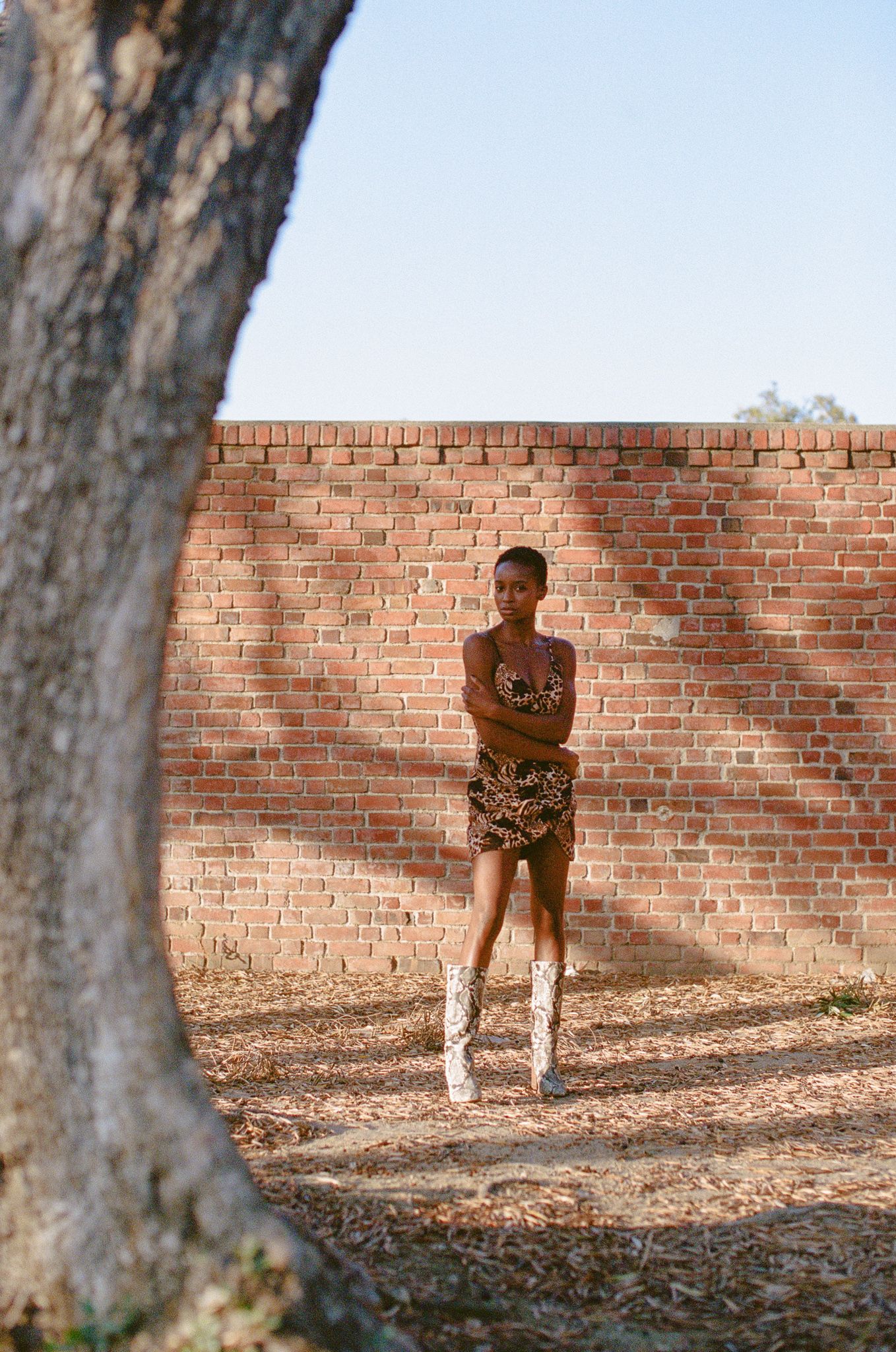 A model poses against a brick wall wearing a patterned outfit and white boots.