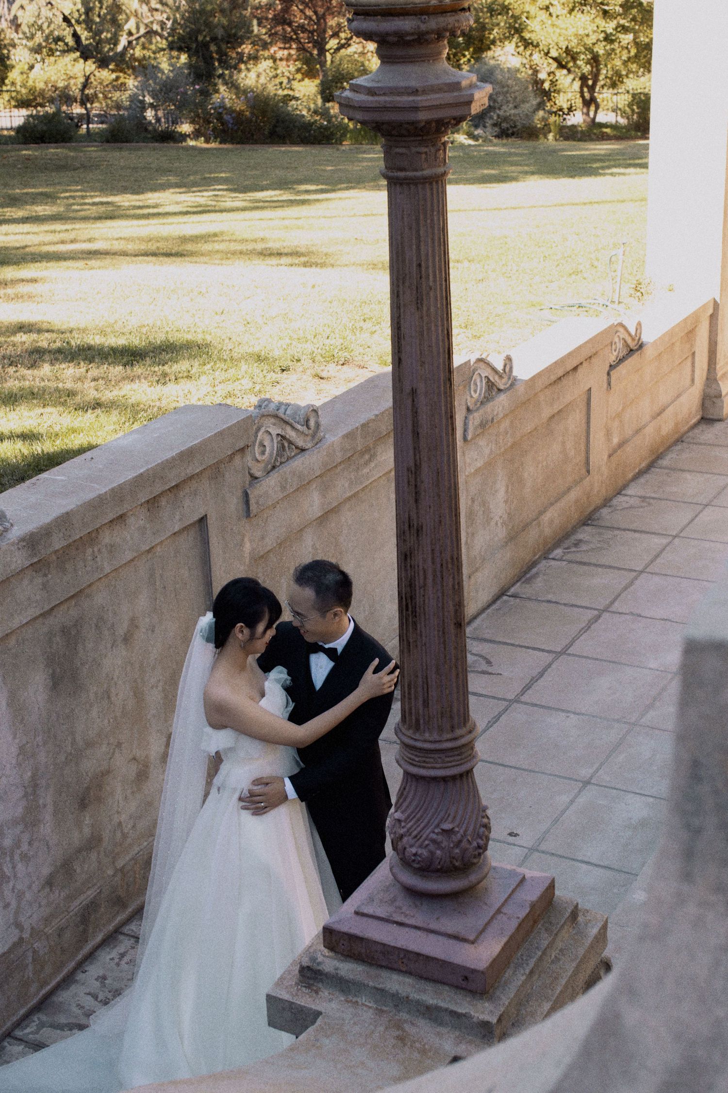 A romantic wedding moment captured between a couple by an ornate stone pillar.