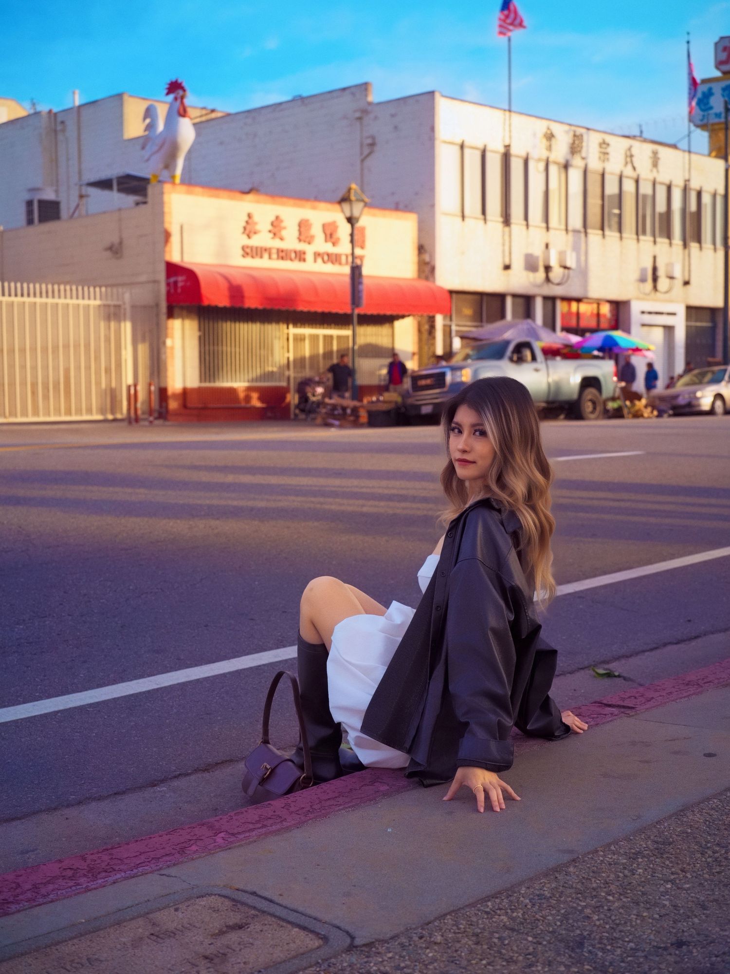 Model sits on sidewalk in urban setting with Chinese restaurant storefront.